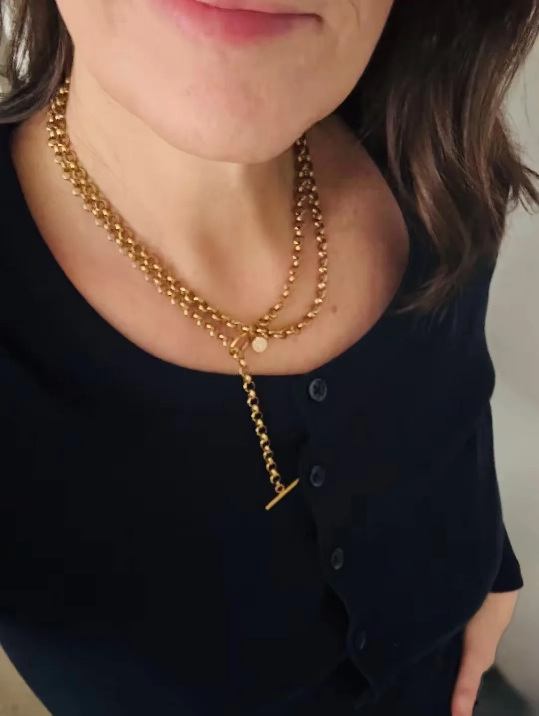 Close-up of a woman's neck wearing Chain Rule's Wrap Lariat gold necklace, with a blue top featuring buttons.