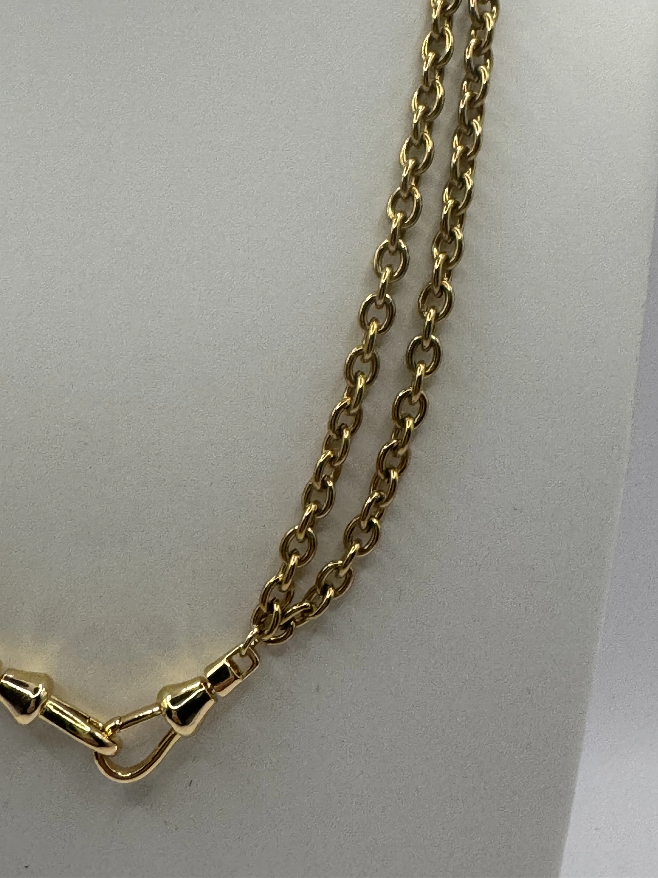 Close-up of a gold chain necklace with a clasp on a plain, off-white surface.
