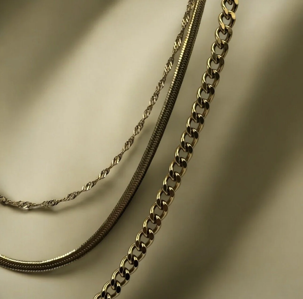 Three gold necklaces layered one with small teardrop pendants, one with pearls on a white display bust. They are available from Chain Rule Jewellery.