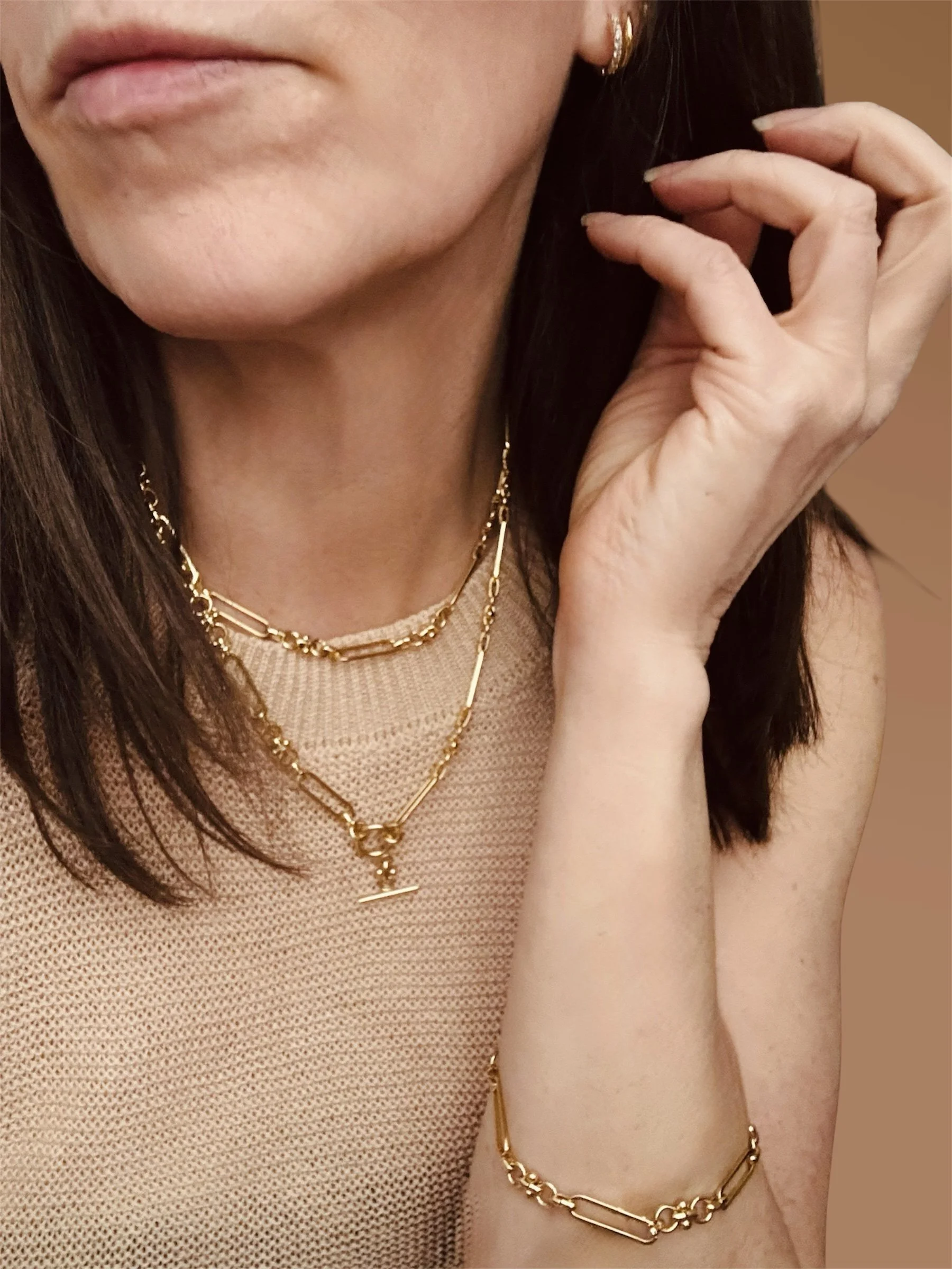 Three gold necklaces layered one with small teardrop pendants, one with pearls on a white display bust. They are available from Chain Rule Jewellery.