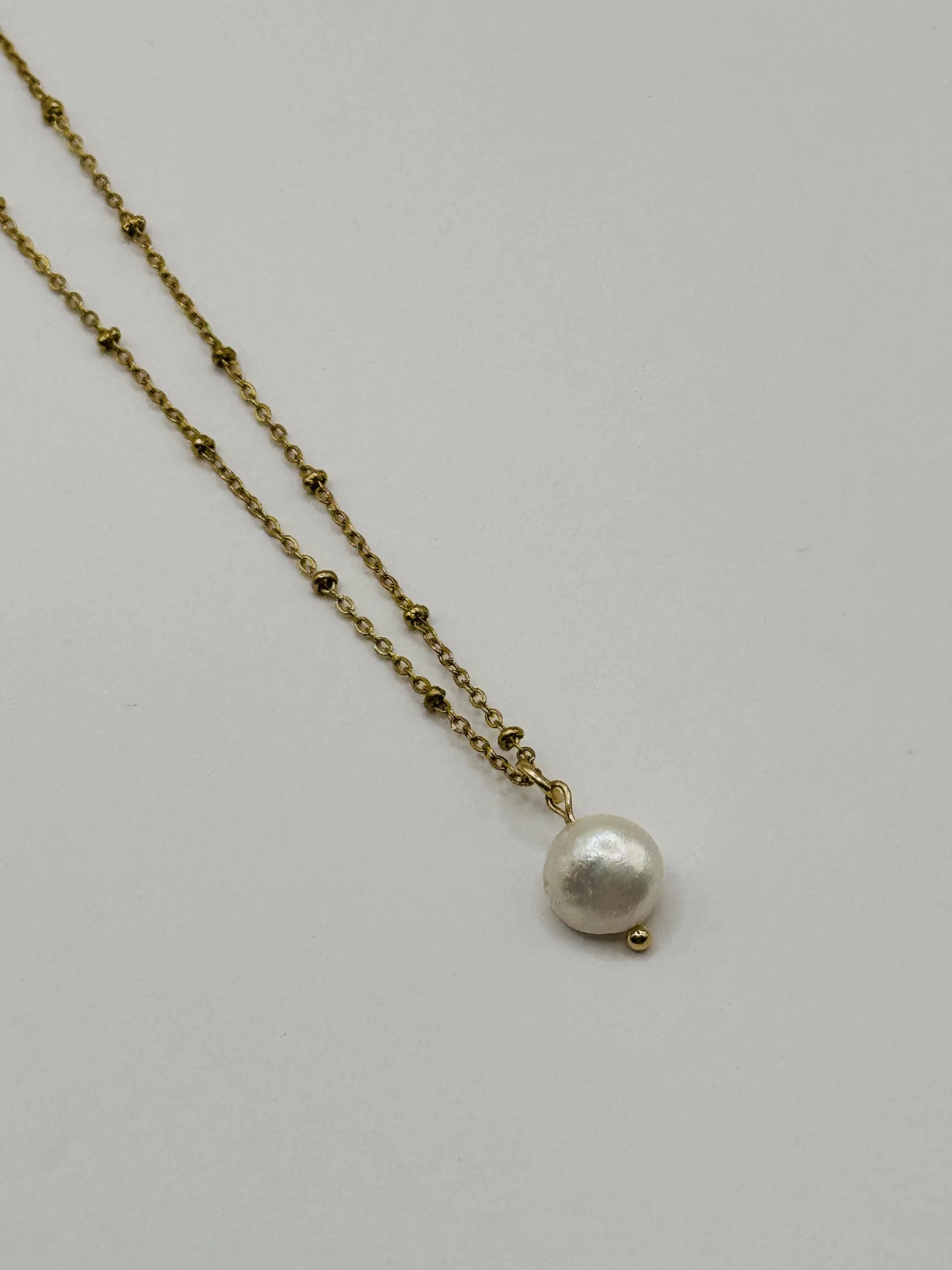 Gold chain necklace with a large white pearl pendant and a small gold bead. Available from Chain Rule Jewellery.