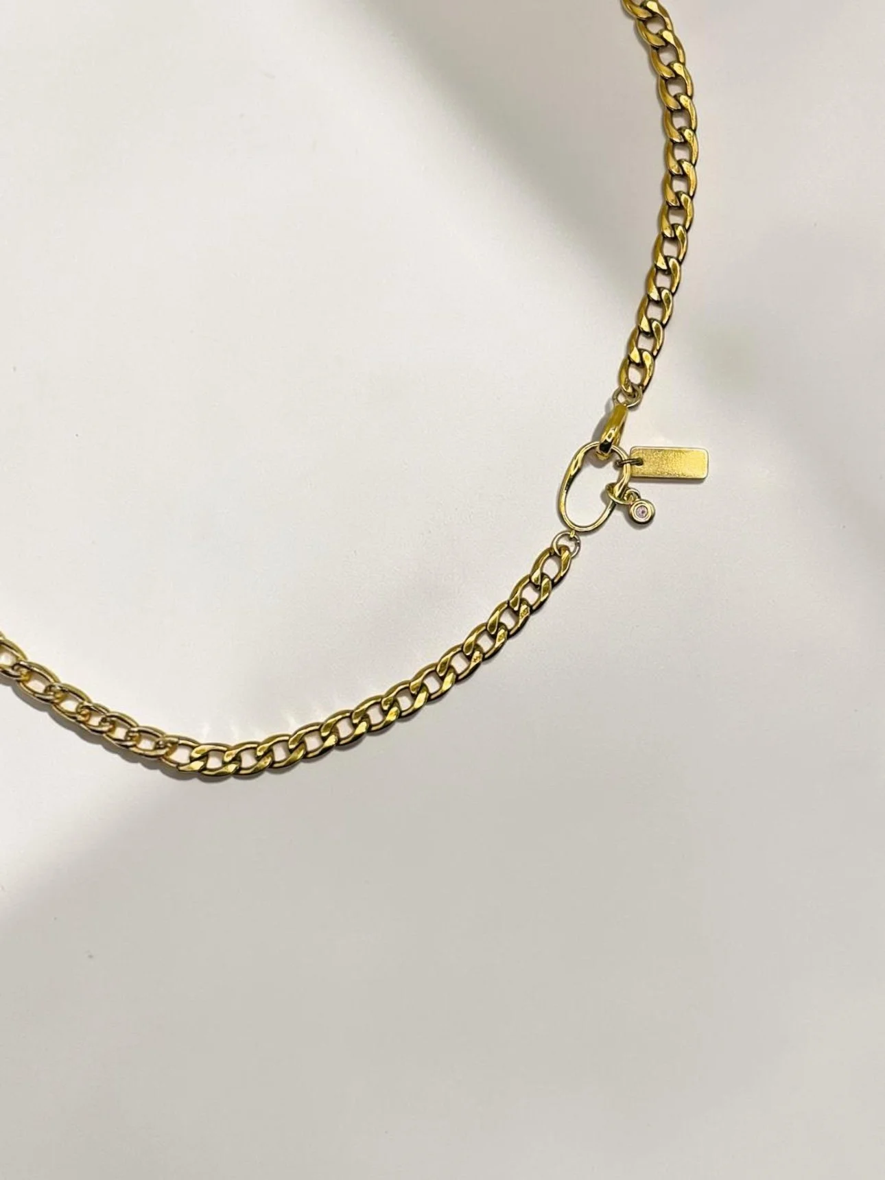 Gold curb necklace with two small charms on a white mannequin bust