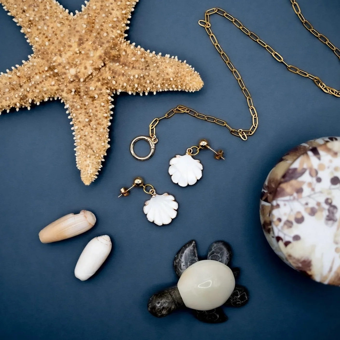 Starfish, gold chain necklace, shell earrings, seashells, polished stone turtle figurine, decorative stone.