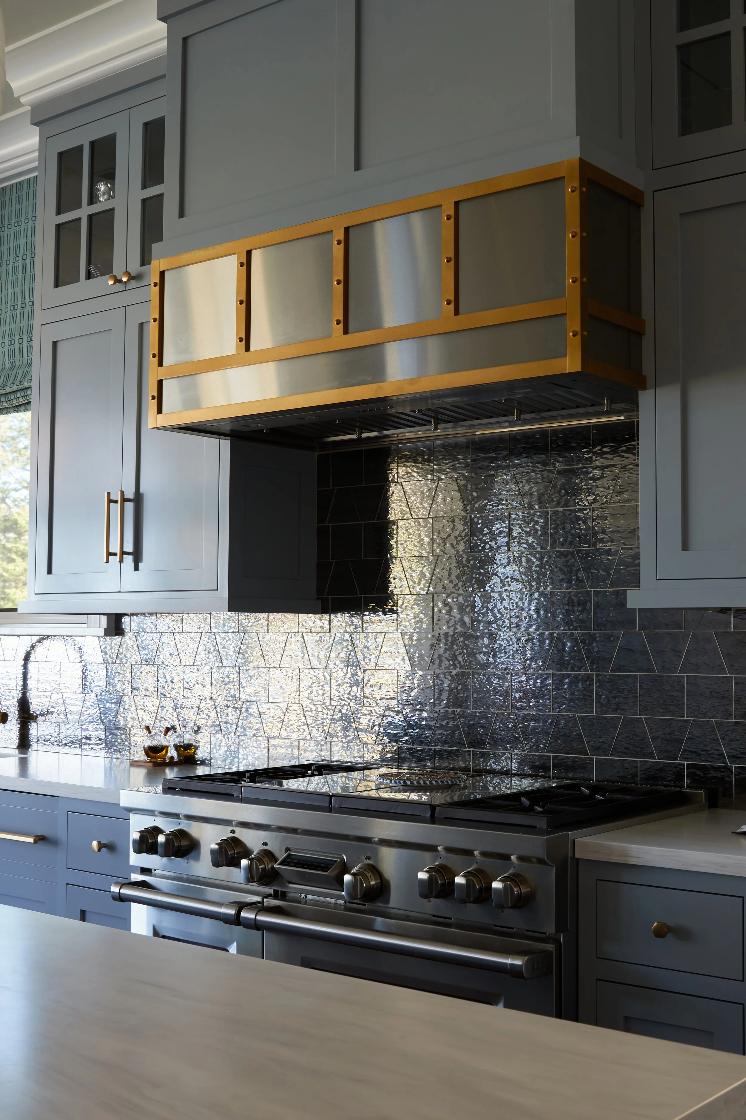 Modern kitchen with blue cabinets, black tiled backsplash, a stainless steel stove, and a wooden and metal vent hood.