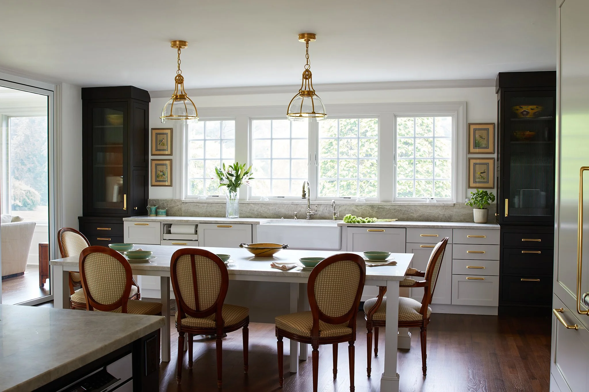 Bright kitchen with white cabinets, large windows, and a wooden dining table with six chairs decorated with a bowl, plates, and utensils.