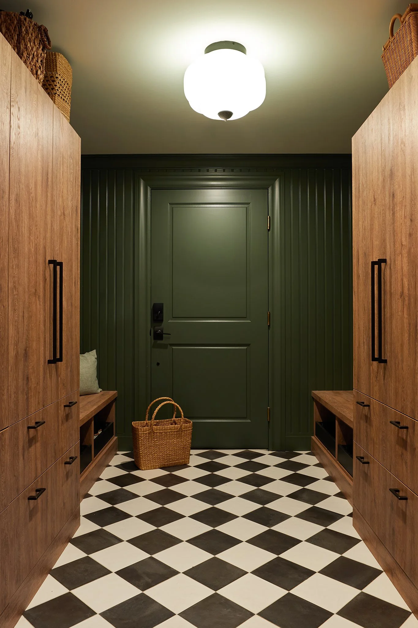 Entryway with black and white checkered floor, green door, wooden storage units, and a woven basket on the floor.