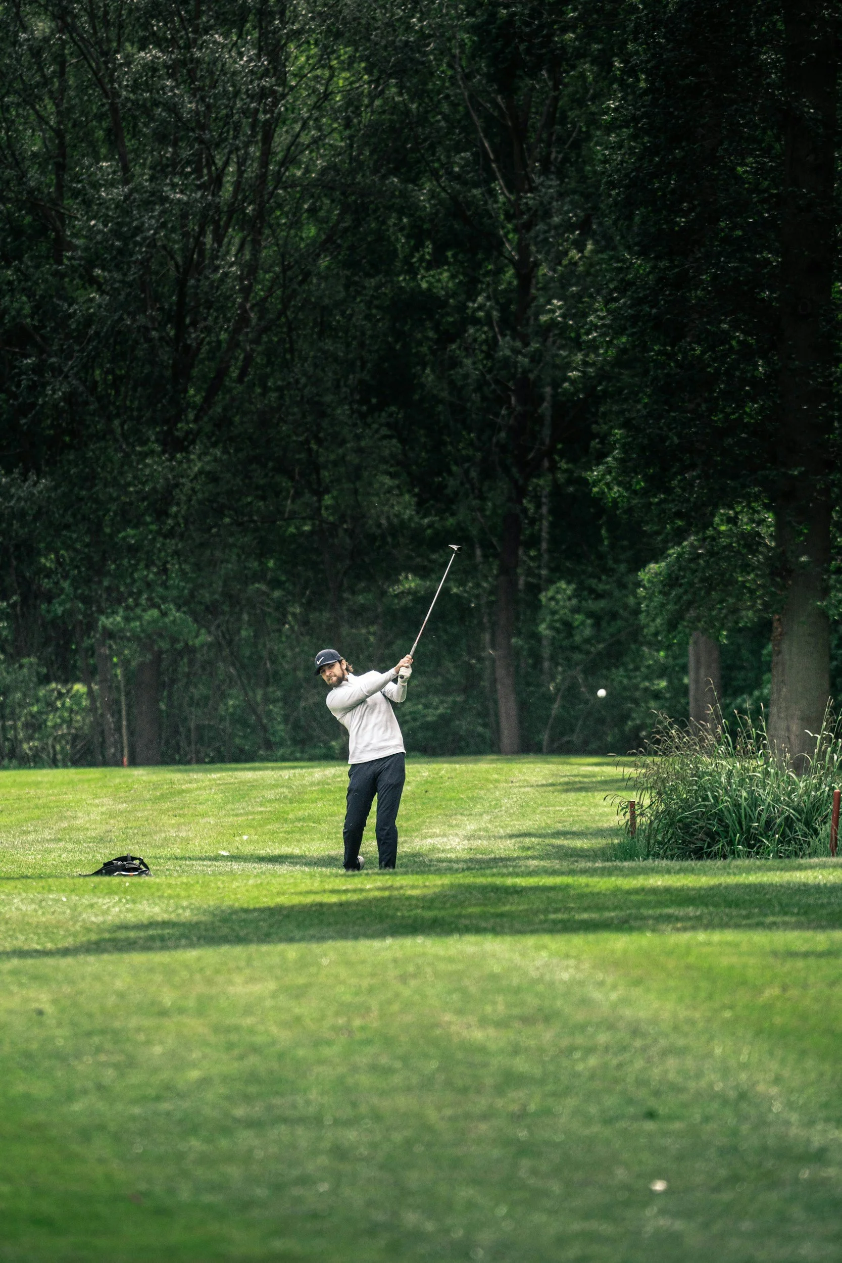 A man playing golf on a lush green golf course, swinging a golf club with a golf ball in midair.