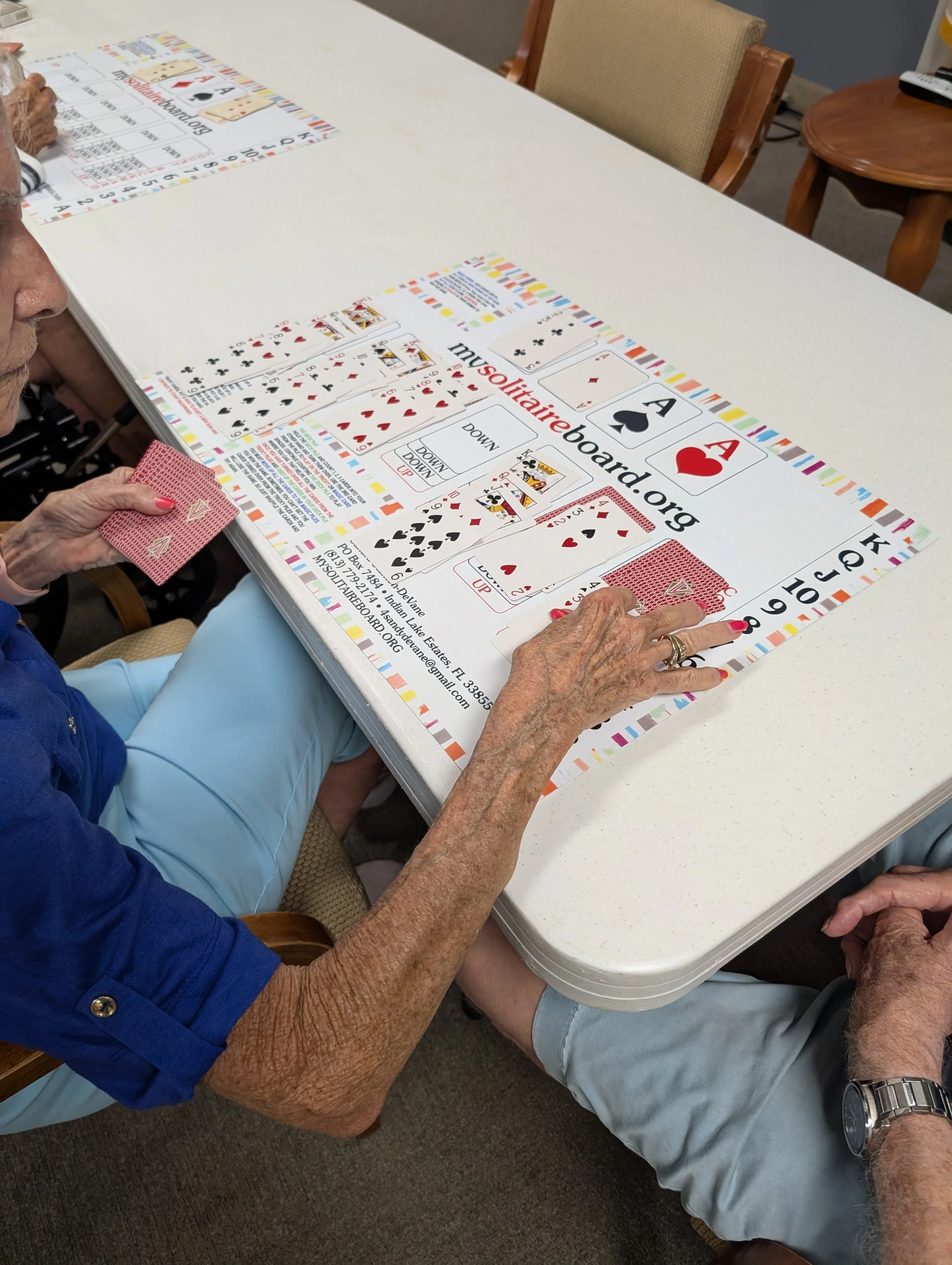Two elderly women are playing a Janie's Game, an accessible Solitaire board designed for individuals with Down syndrome, autism, seniors, and caregivers.