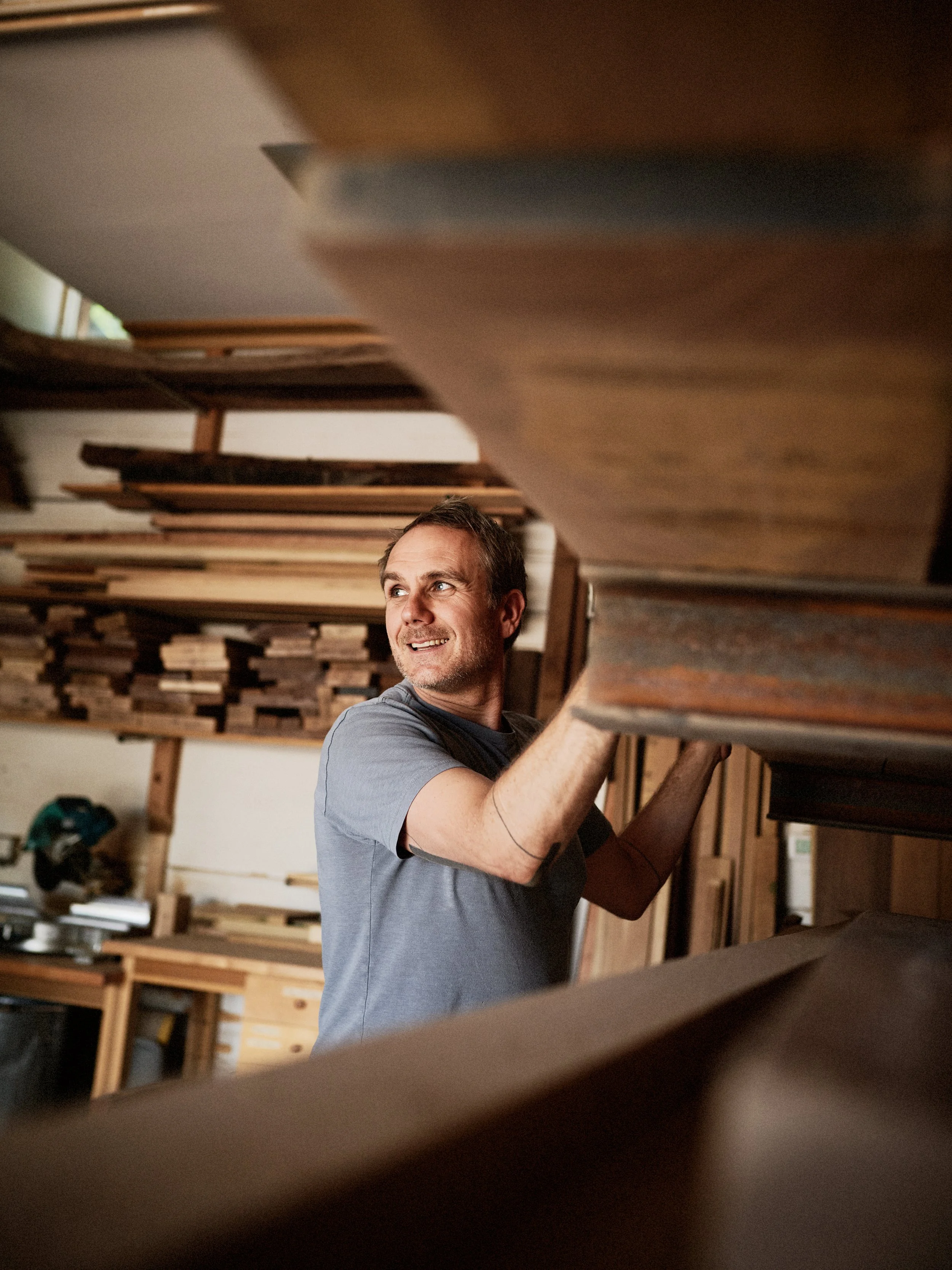 Man working in a woodworking shop, lifting or adjusting a wooden piece.