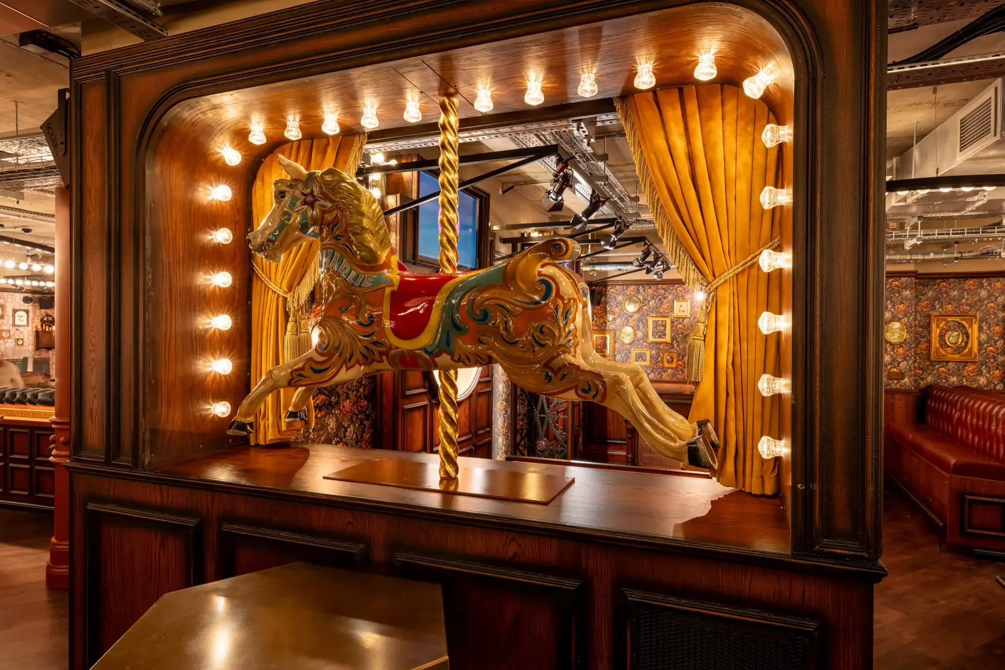 Carousel horse feature inside Flight Club, lit with warm bulbs and framed by velvet curtains — interior design by Studio Hayes.