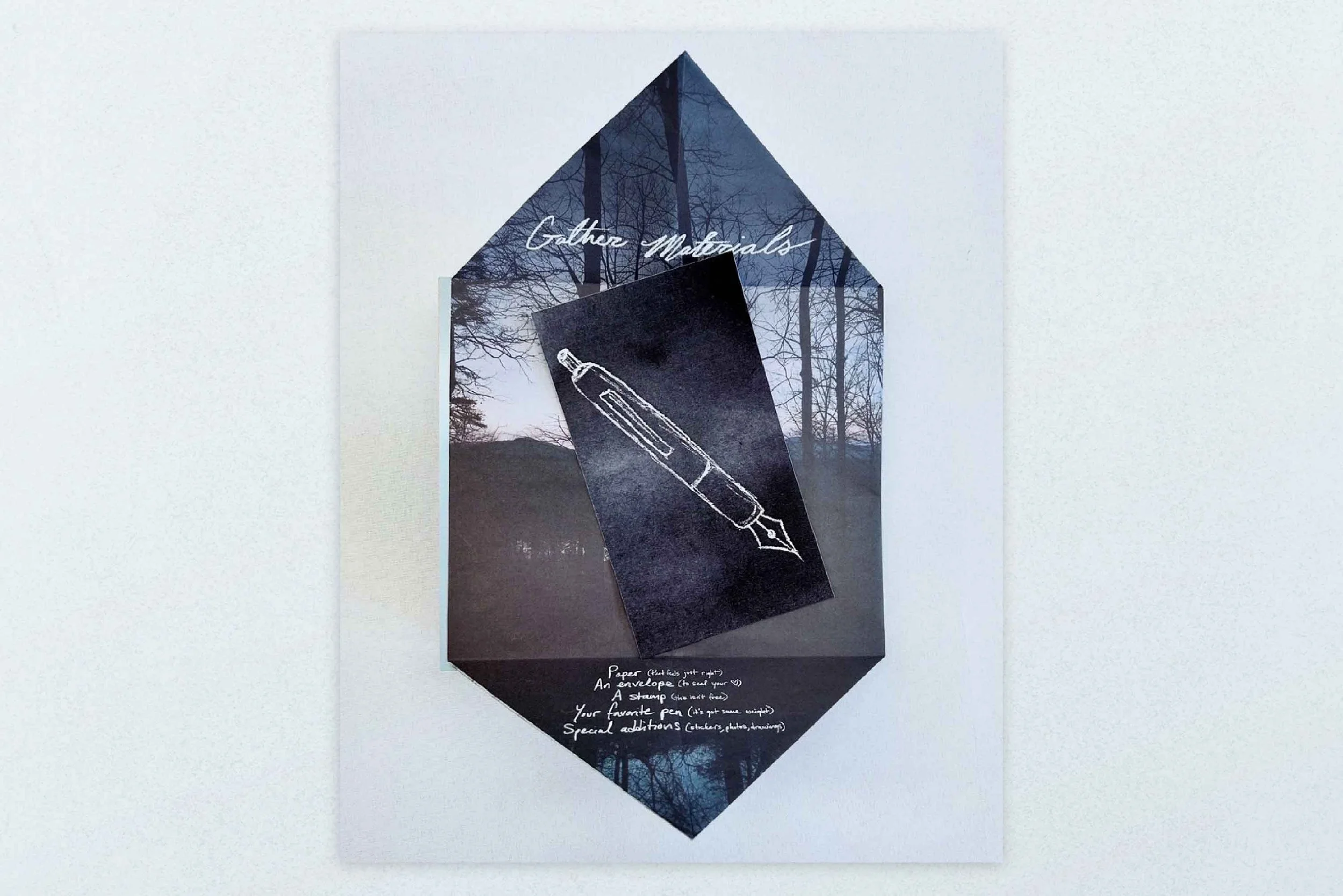 A display with a dark background featuring a woodland scene and white handwritten text, including a sketch of a fountain pen. The text reads 'Gather Materials' at the top, and additional notes at the bottom about paper, envelopes, a favorite pen, and