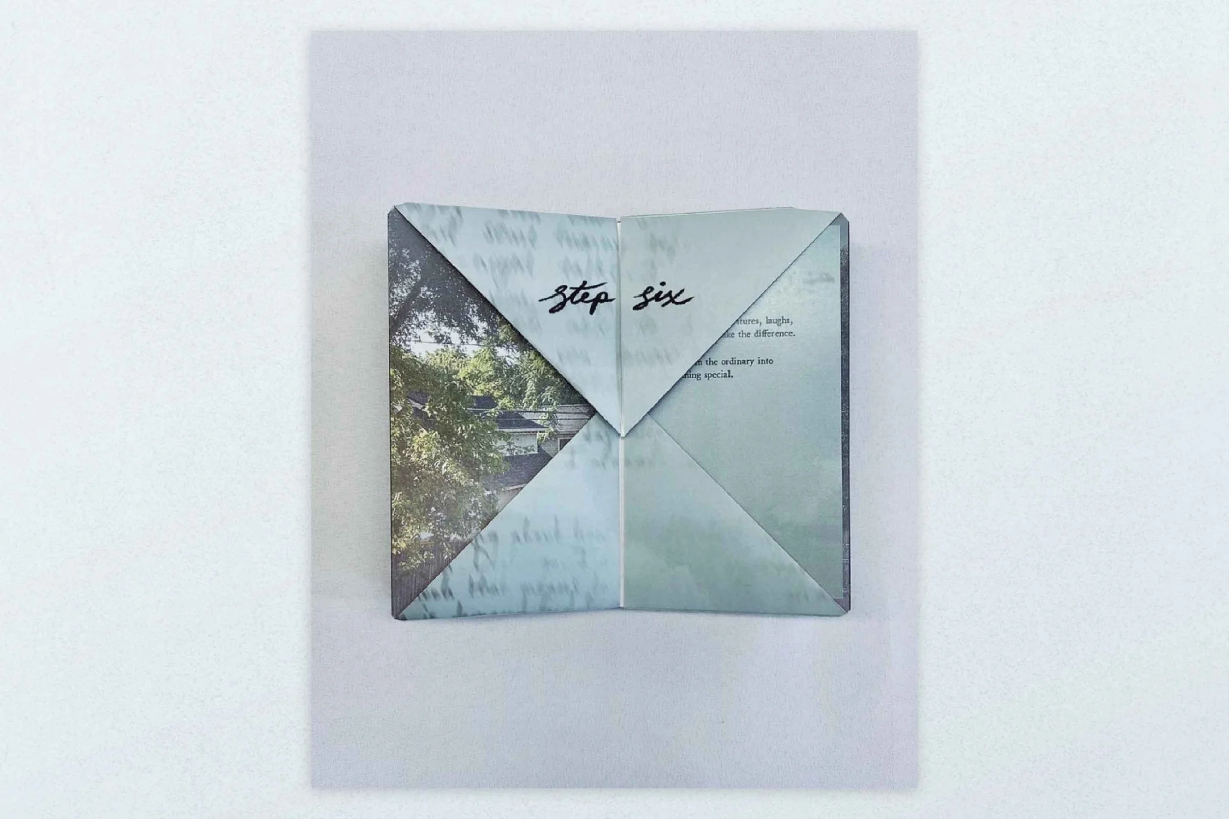 An open folded paper with the words "stop six" written on the center flap, revealing a background with greenery and a house.