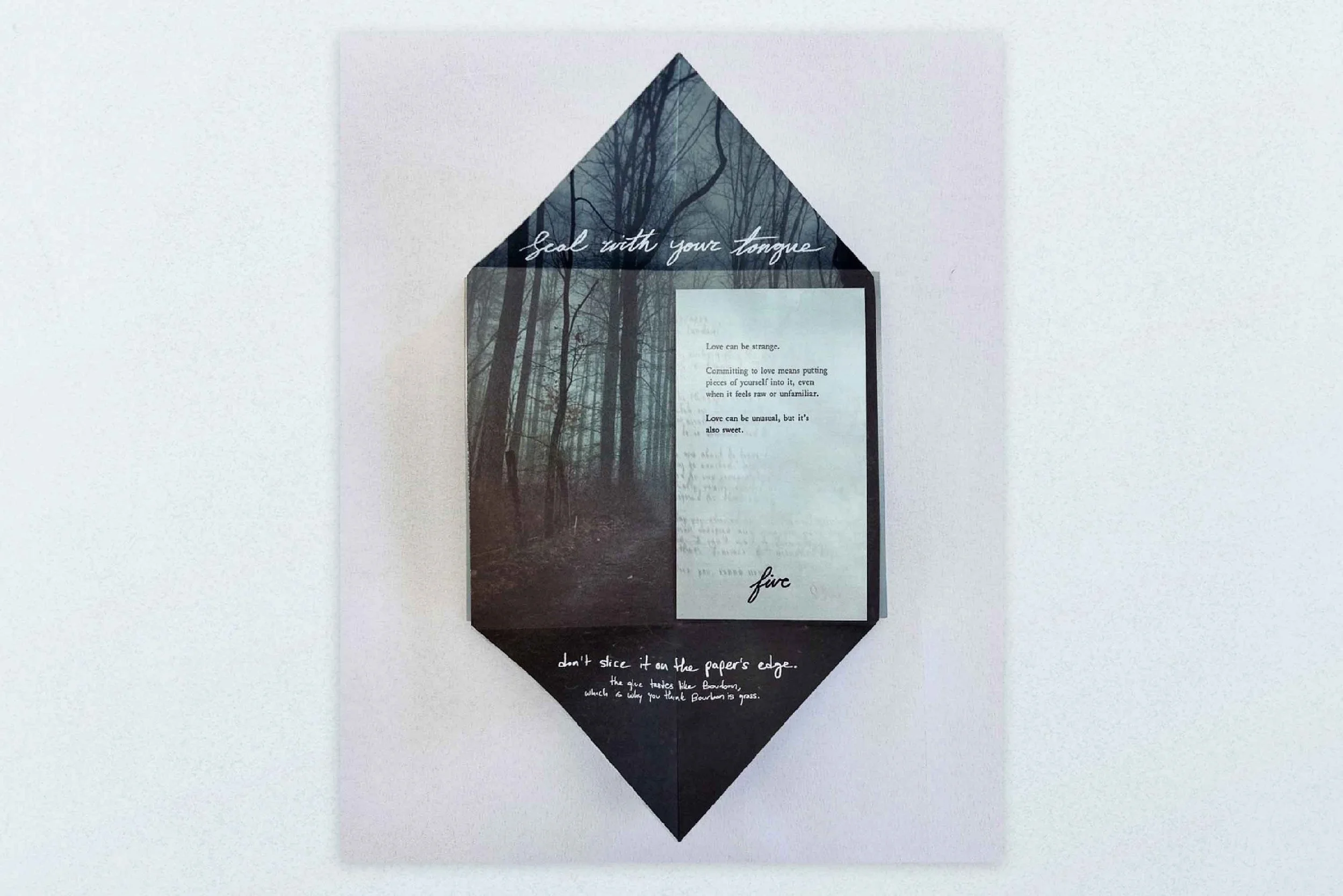 A paper craft with a dark forest background and white handwritten text, including phrases like 'Seal with your tongue' and 'don't slice it on the paper's edge.'