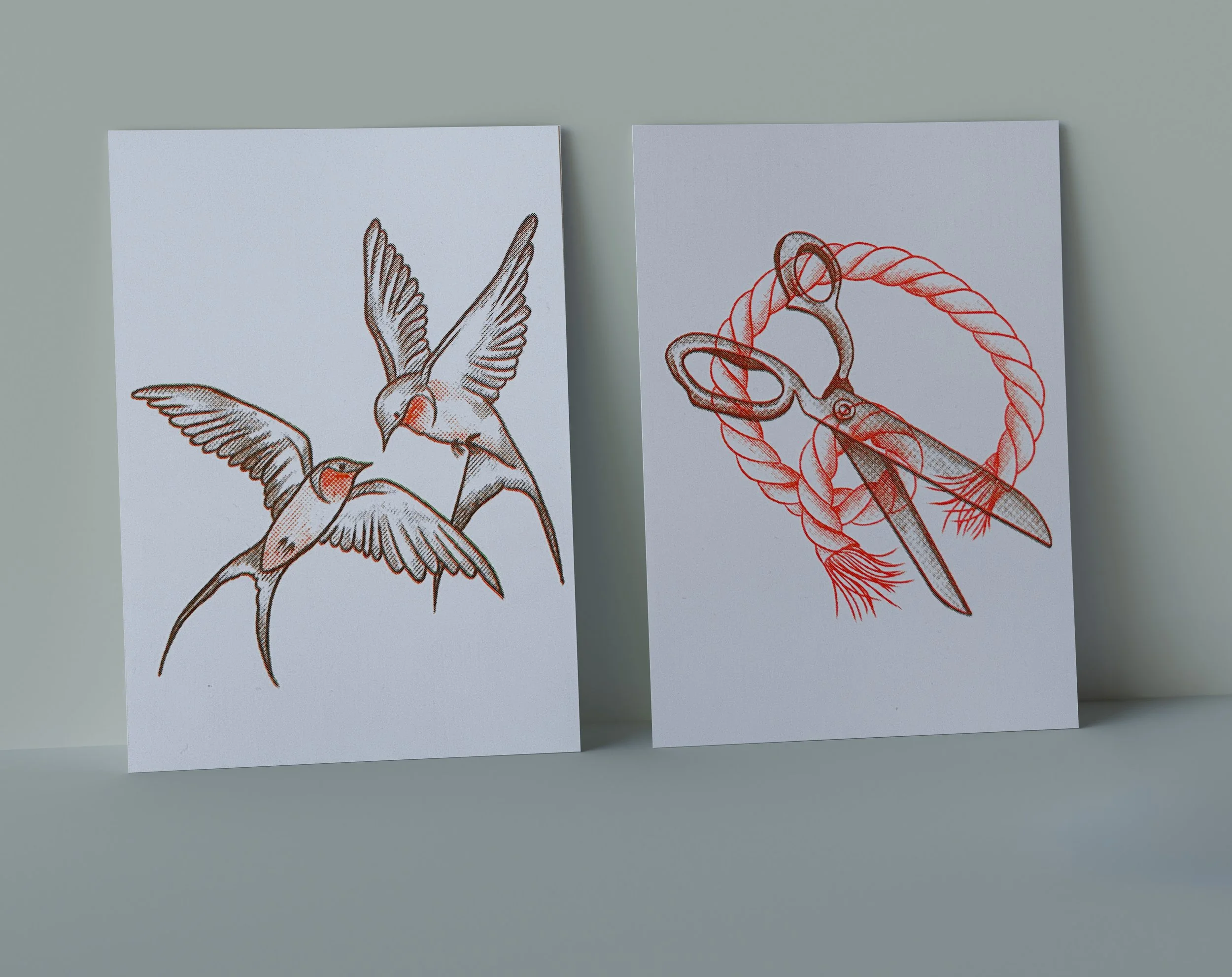 Two sheets of paper with tattoo-style illustrations, one depicting flying birds and the other showing a pair of scissors and a fish with a rope.