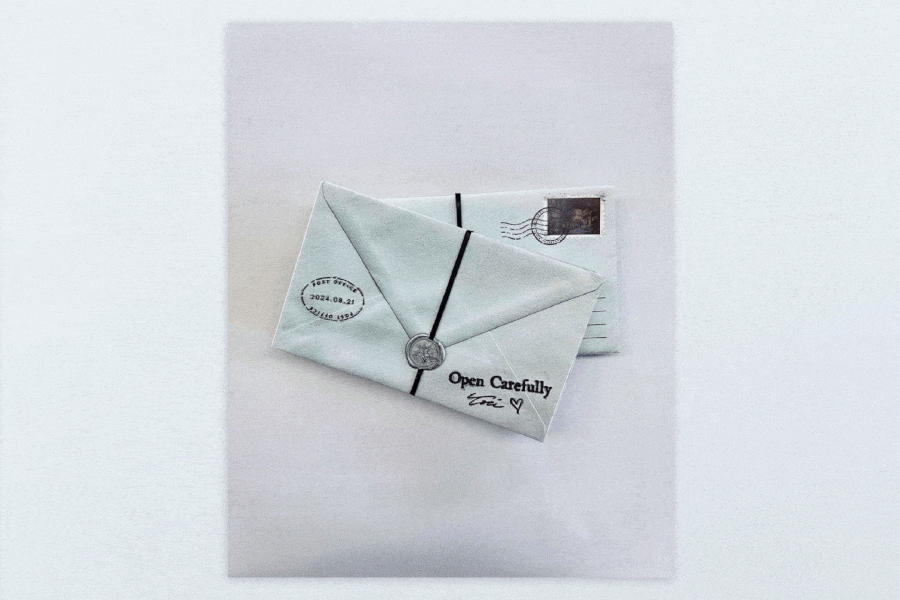 A white envelope with a black string tying it and a wax seal in the middle, along with a letter with a postmark, and a handwritten note that says "Open Carefully Ellie" with a heart symbol.