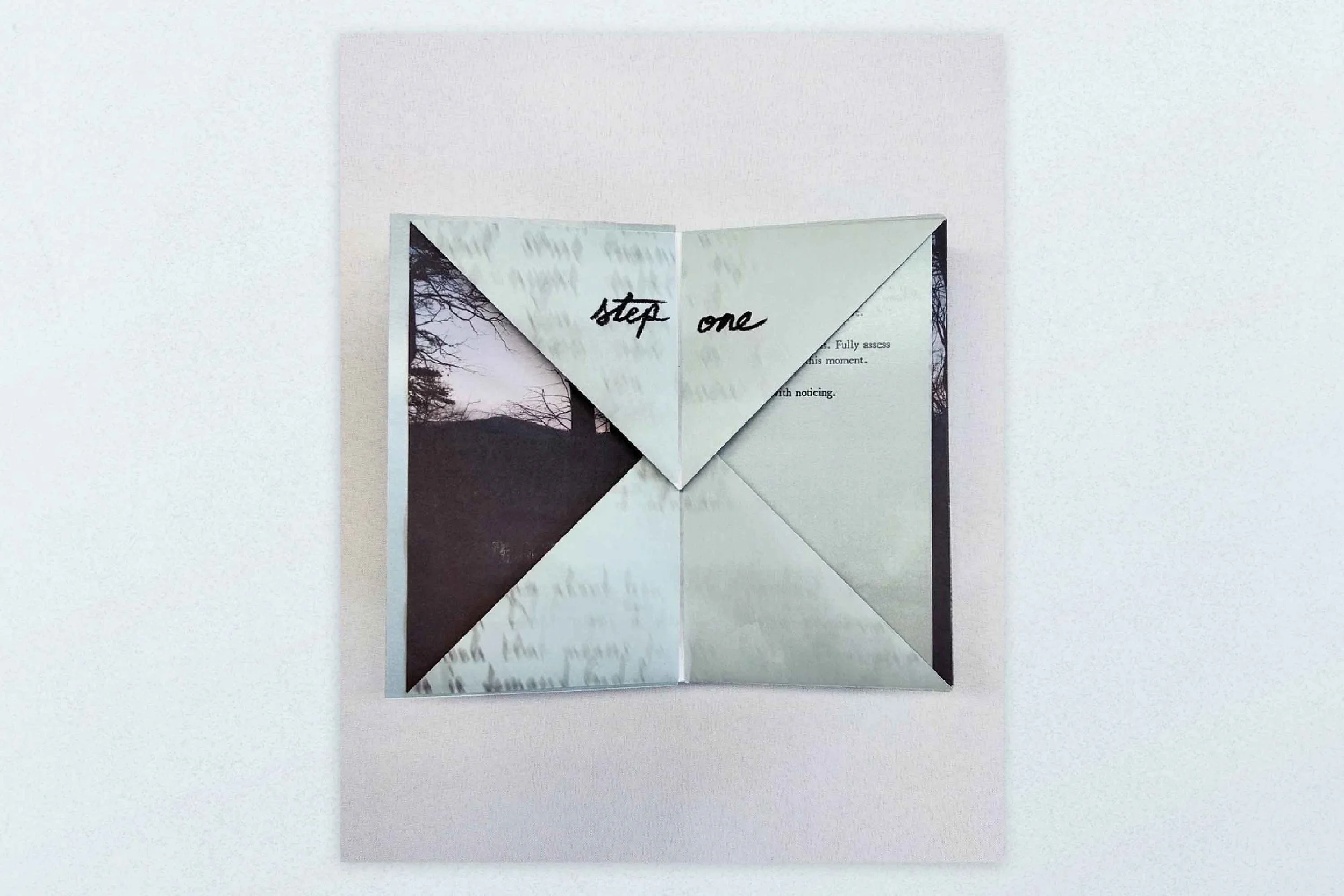 A folded paper with handwritten text 'step one' on top, revealing a black and white photograph of trees and hills beneath.