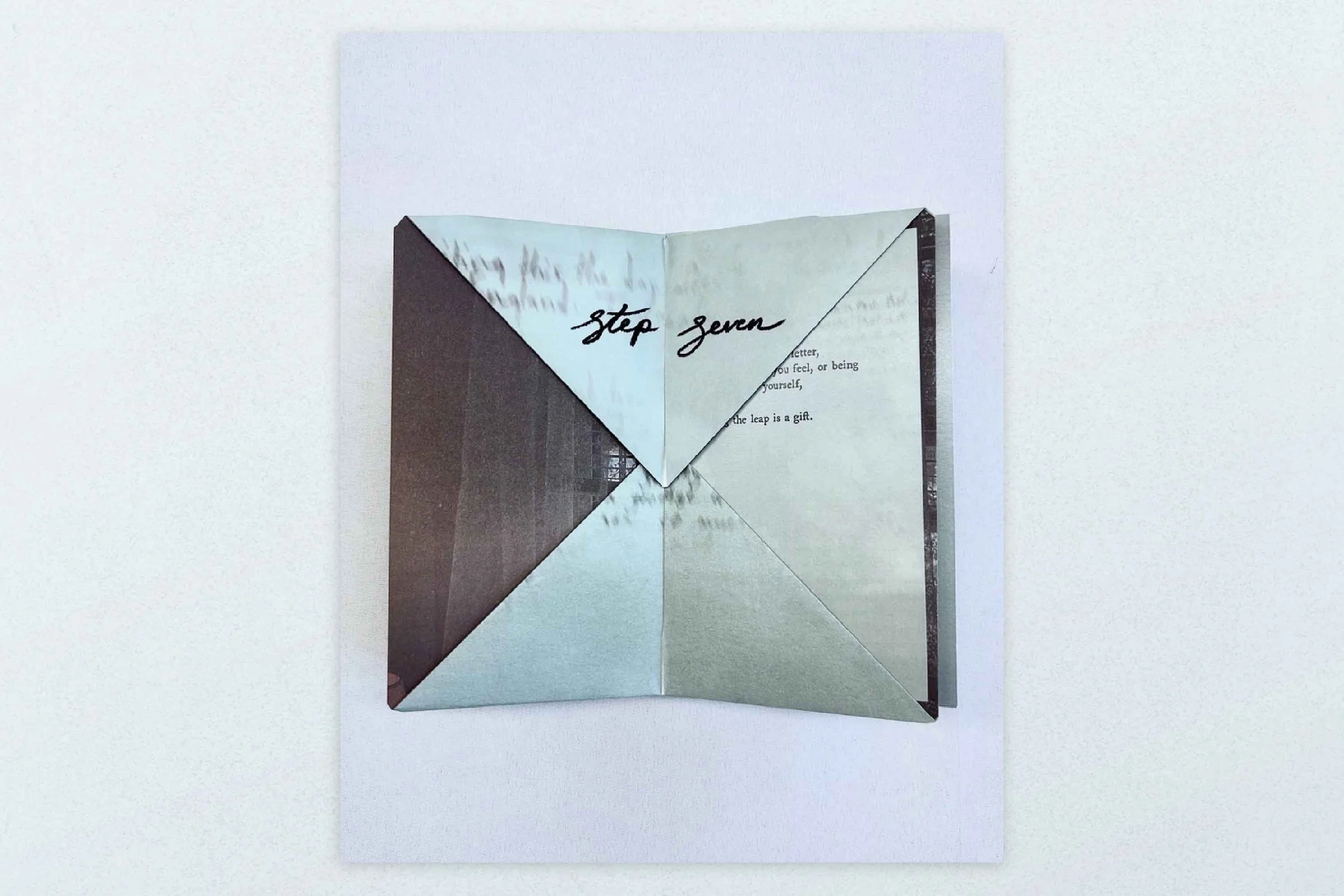An open book with a folded paper overlay showing “step seven” handwritten in black ink.