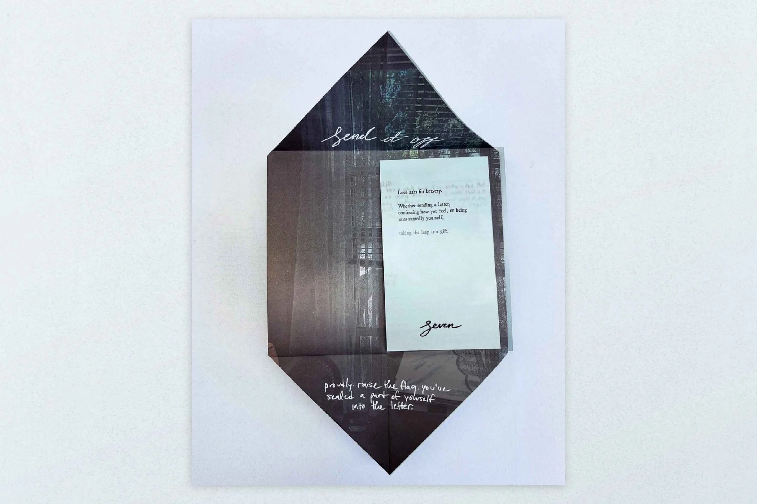 A decorative display with a layered paper art piece resembling a house shape, containing a letter, with the words "send it off" at the top and handwritten notes at the bottom.