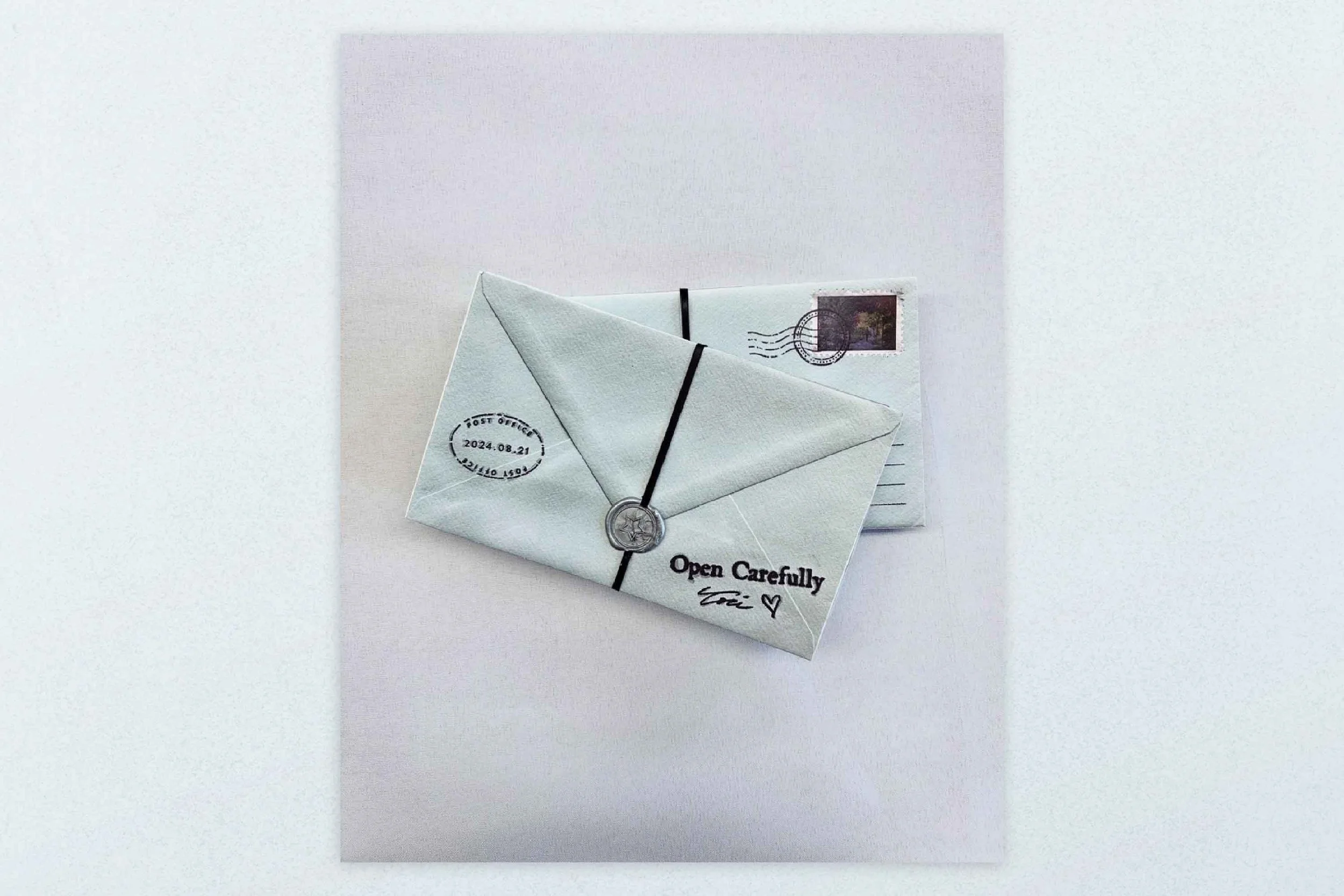White envelope with black string closure and postal cancellation mark, placed on top of a postcard with postage stamp, on a light background.
