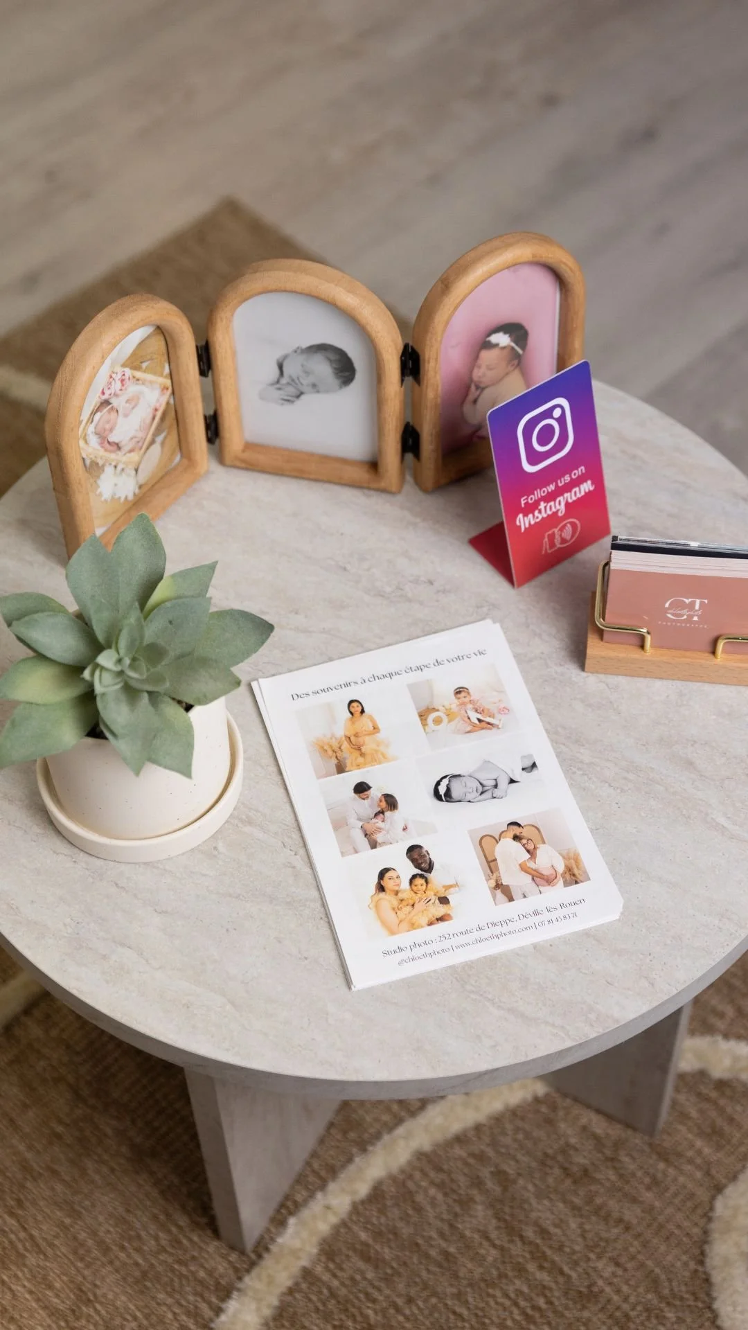 Table avec un cadre photo contenant des images de bébés, une plante succulente, un dépliant promotionnel, une carte de visite, et un signet pour suivre sur Instagram.