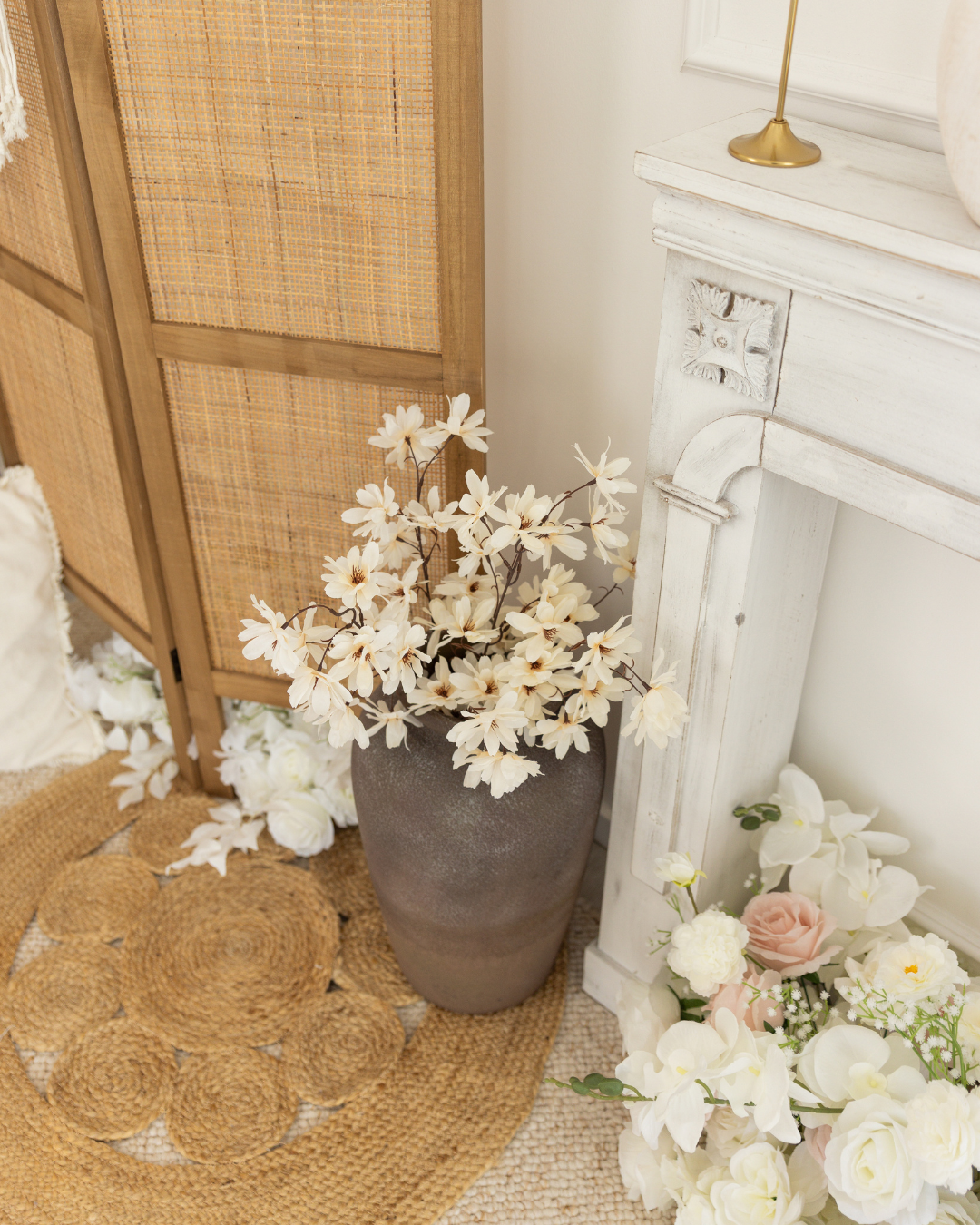 Vase avec des fleurs blanches devant un paravent en bois et un manteau blanc vintage.