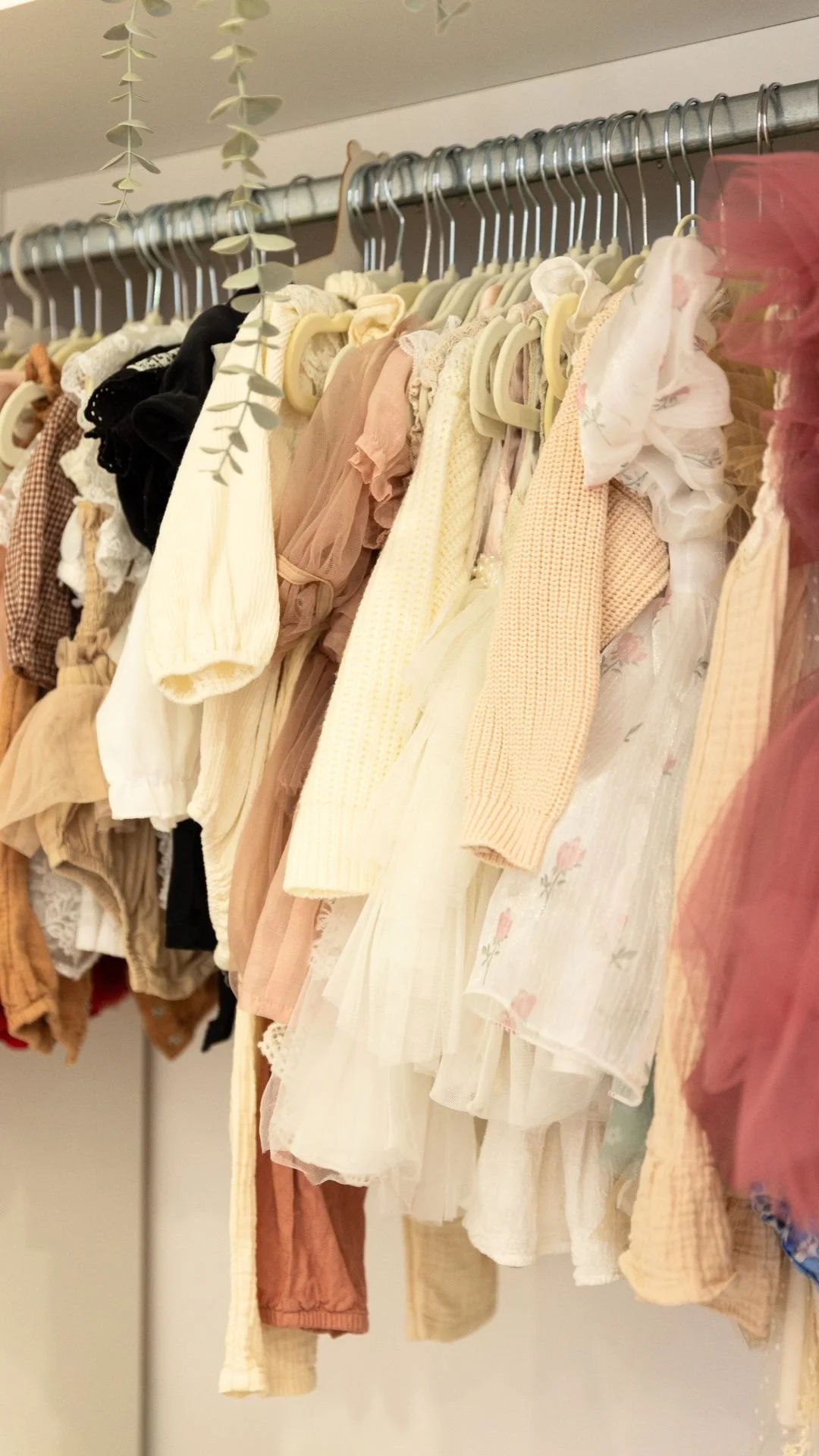 Vêtements pour bébés, comme des robes, des pulls et des pantalons, suspendus sur une barre de garde-robe.