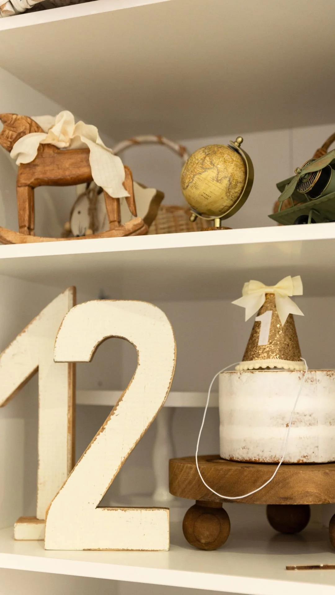 Décor de fête de 1er anniversaire, comprenant une grande chiffre 2 en bois blanc, un chapeau de fête doré avec un ruban blanc, un globe terrestre, et diverses décorations en bois et en papier.