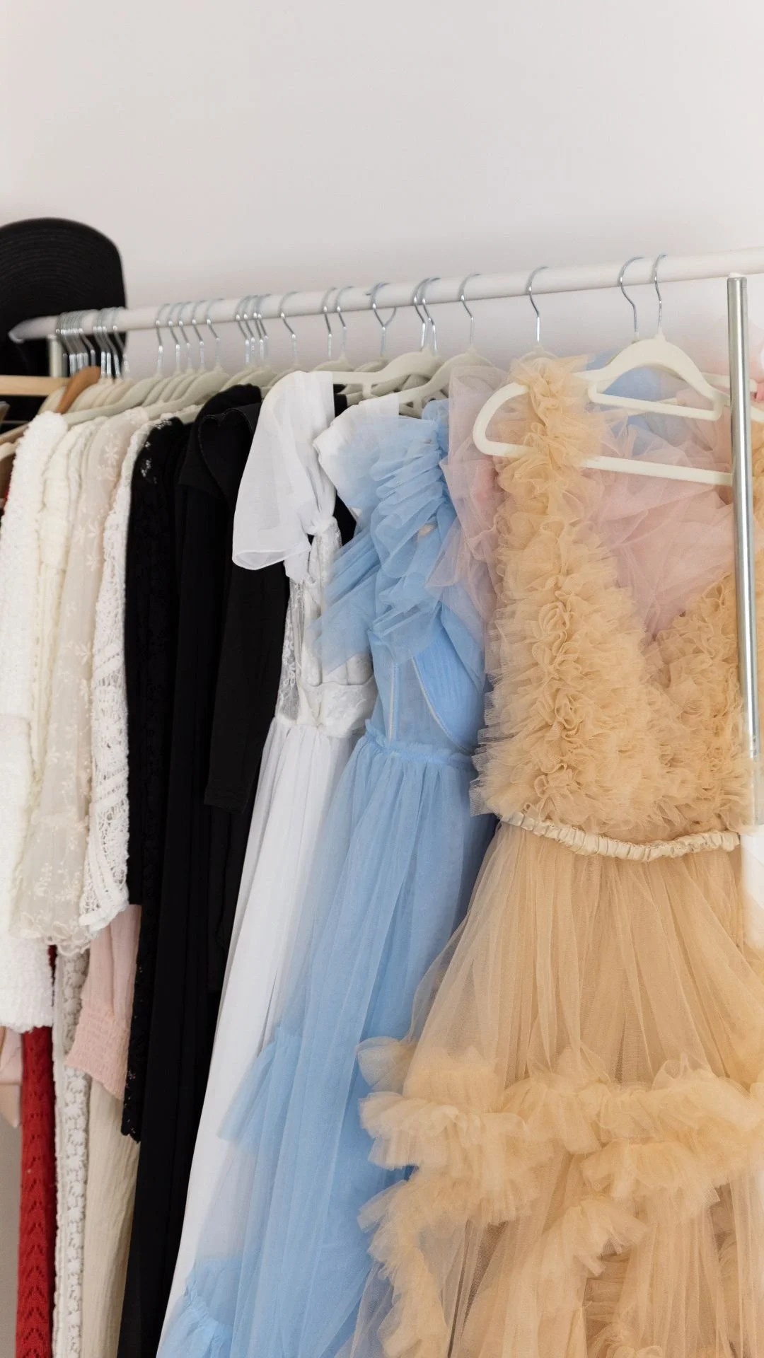 Vêtements pour enfants ou femmes, incluant des robes en tulle bleu et beige, suspendus sur une rack dans une pièce