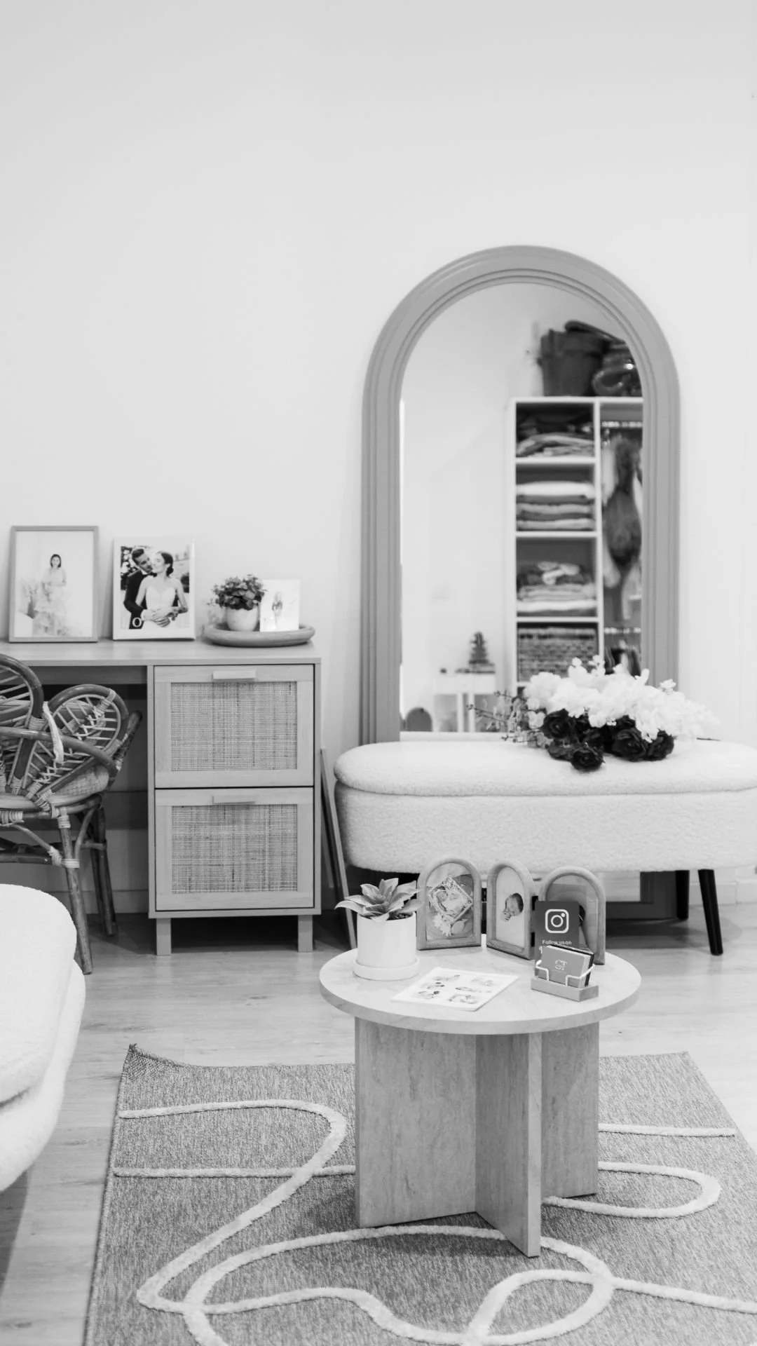 Salon intérieur avec miroir, meubles en bois clair, fleurs sur un canapé en tissu, étagères avec livres et objets décoratifs, tapis avec motif, et photos sur une table