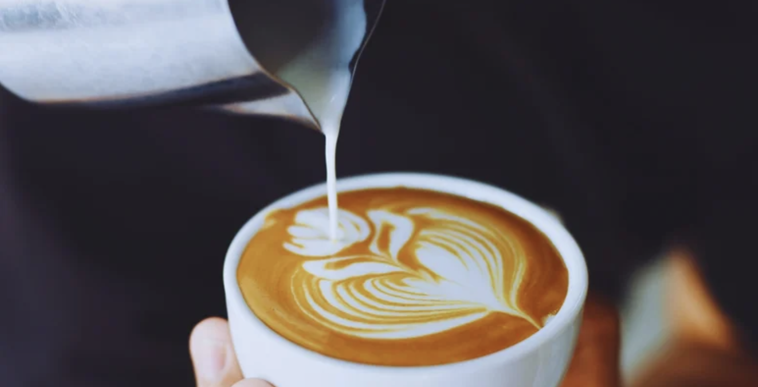 Barista pouring steamed milk into a cup of espresso to create latte art with a floral pattern.