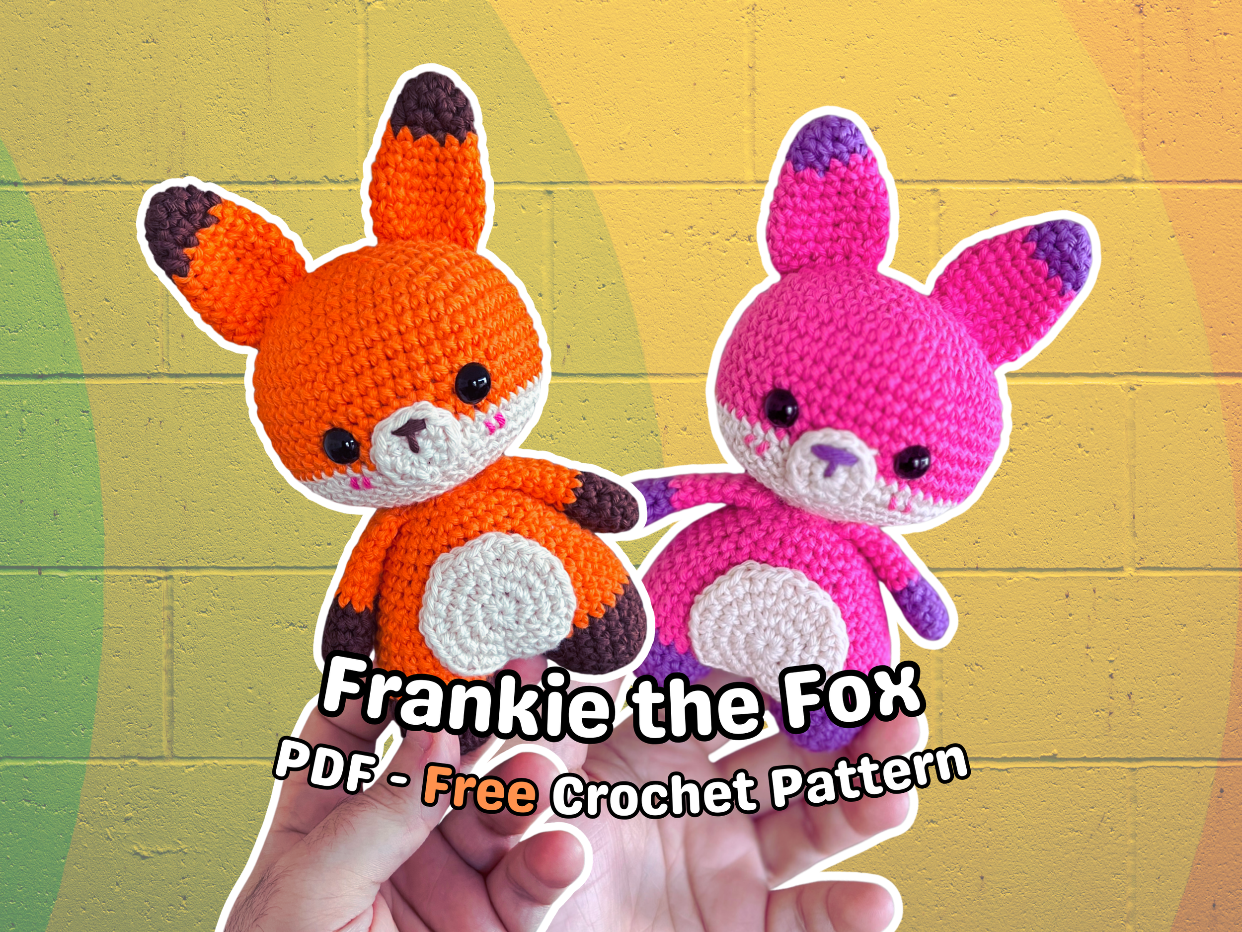 Two crocheted stuffed animals resembling foxes or rabbits, one orange and one pink, are being held in a person's hand against a yellow brick wall background. The text on the image reads: "Frankie the Fox PDF - Free Crochet Pattern."