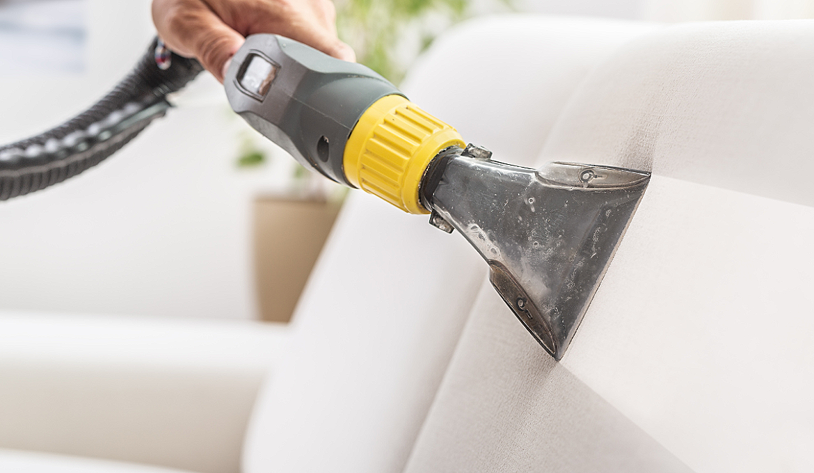 Une main utilise un aspirateur pour nettoyer un canapé blanc.
