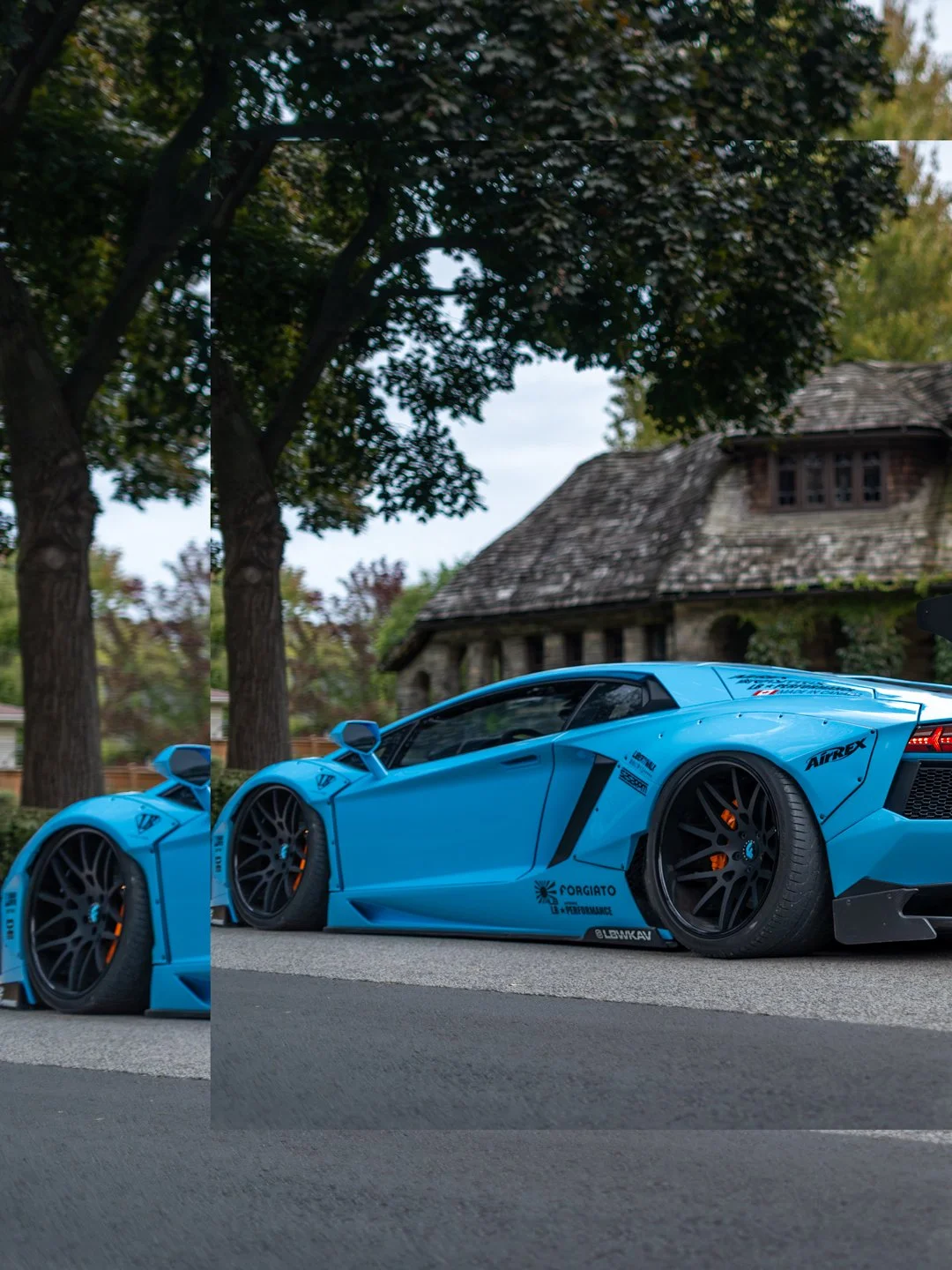 A blue Lamborghini sports car parked on a street with trees and a house in the background.