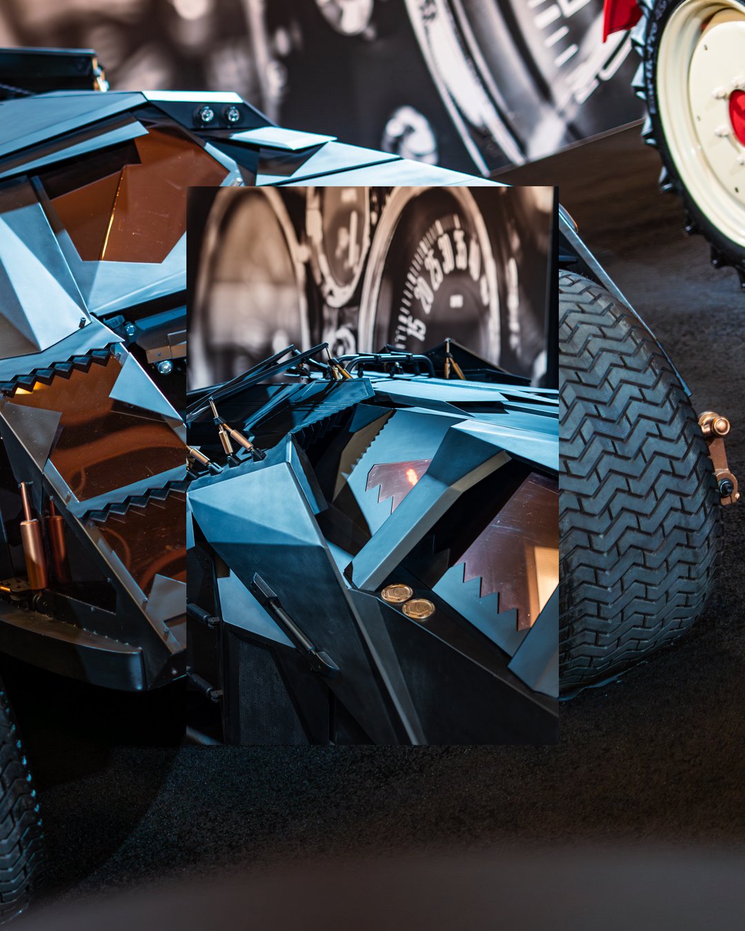 A detailed close-up of the Batmobile from the Batman franchise, featuring angular, metallic blue and black surfaces with sharp edges, and a large rugged tire on the right side. The background includes a blurred dashboard image.