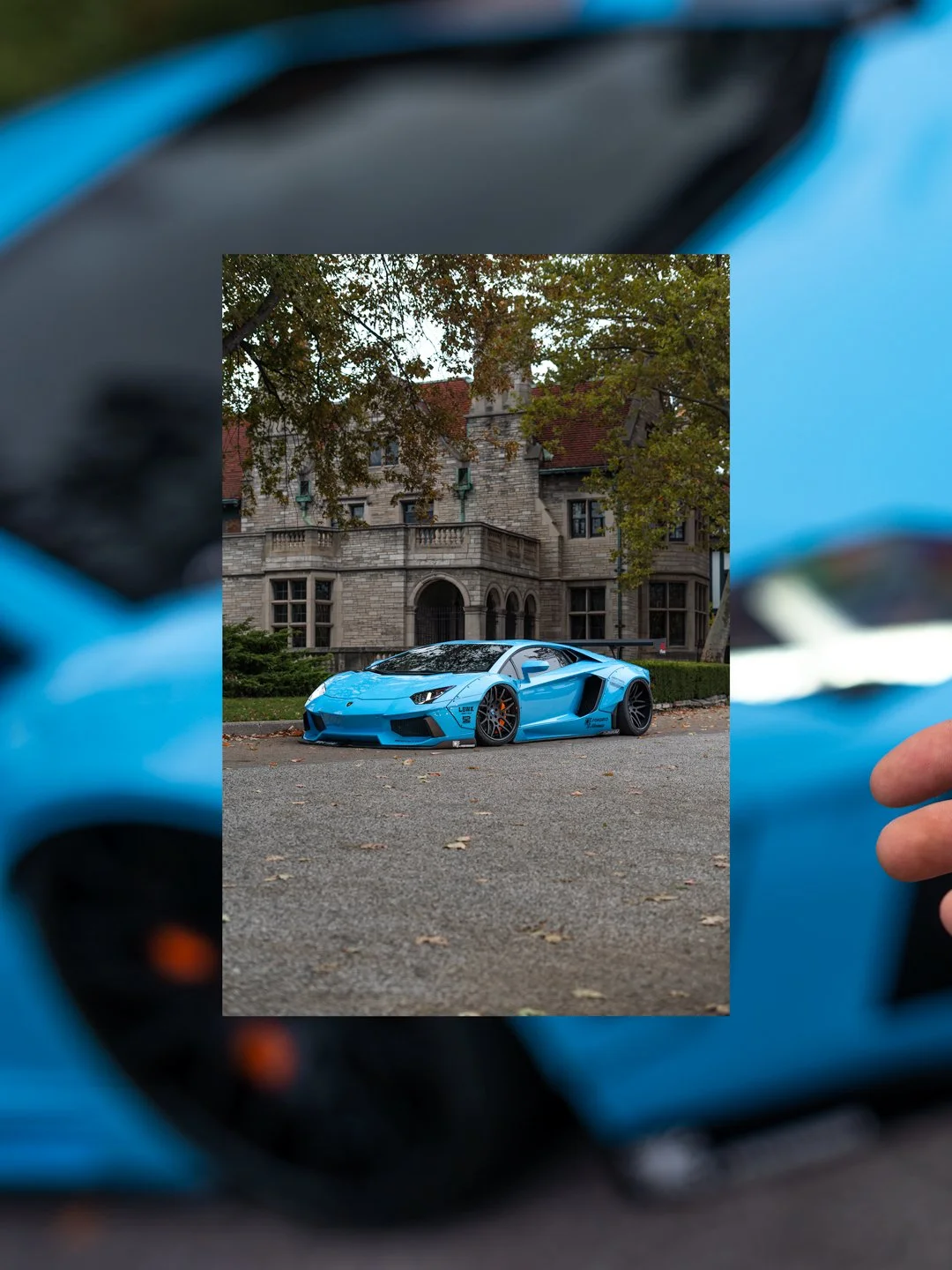 A blue Lamborghini sports car parked in front of a large stone mansion with trees.