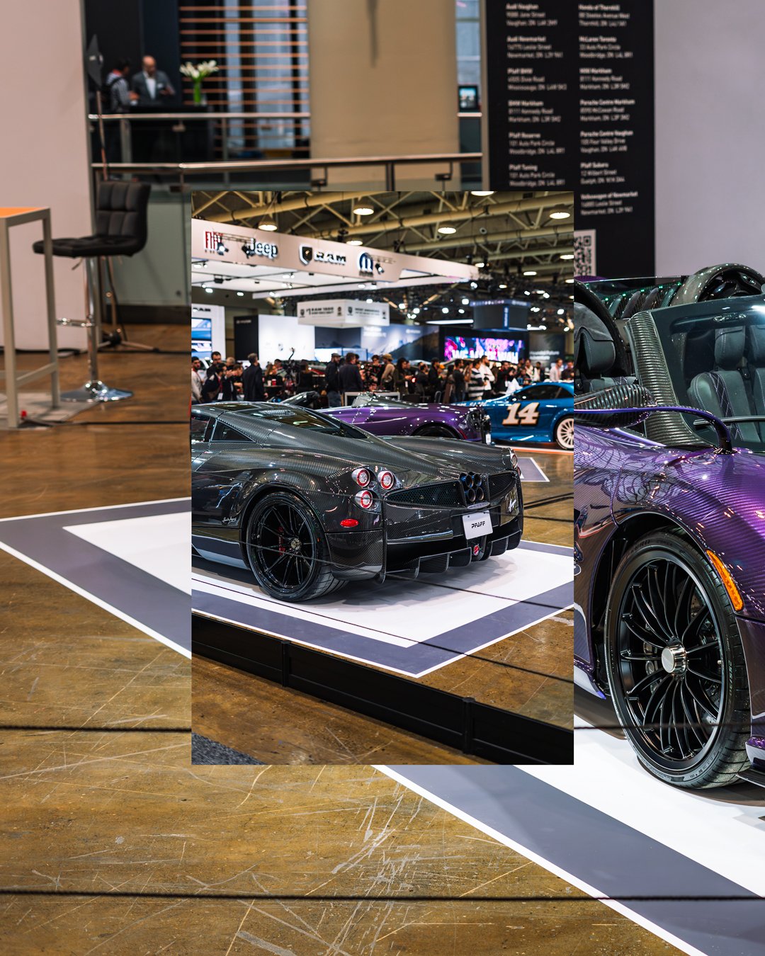 Display of luxury sports cars at an auto show, with one prominent black sports car in the foreground and other vehicles and people in the background.