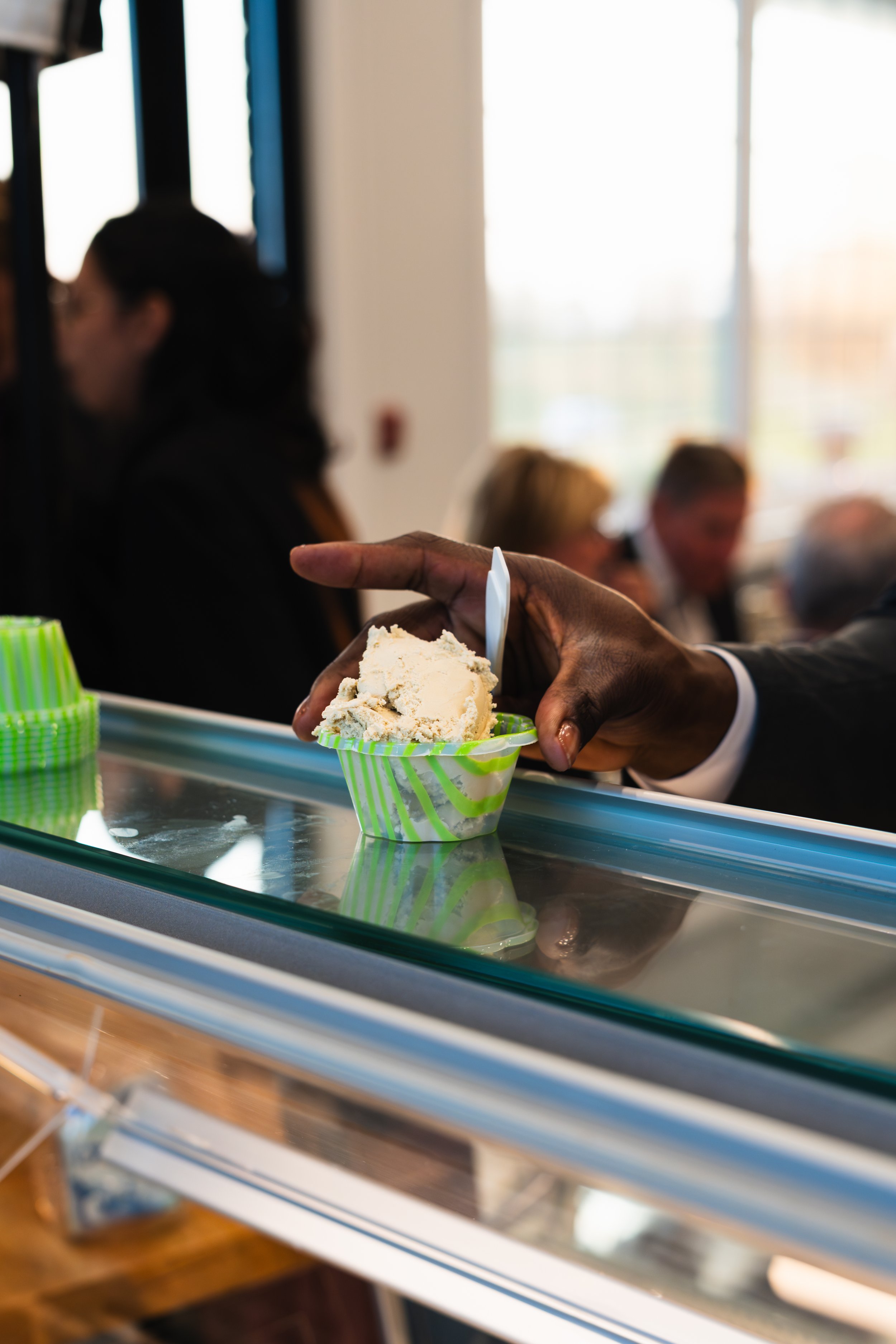 A person is serving ice cream from a container in rows of green and white striped cups behind a glass display case in an ice cream shop.