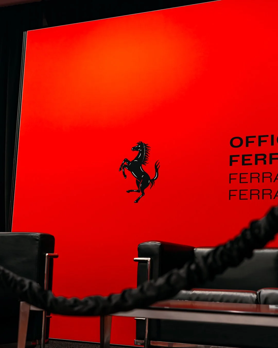 Red wall with a black prancing horse logo and text that reads "OFFIC FERRARI" and repeated "FERRARI" in black.