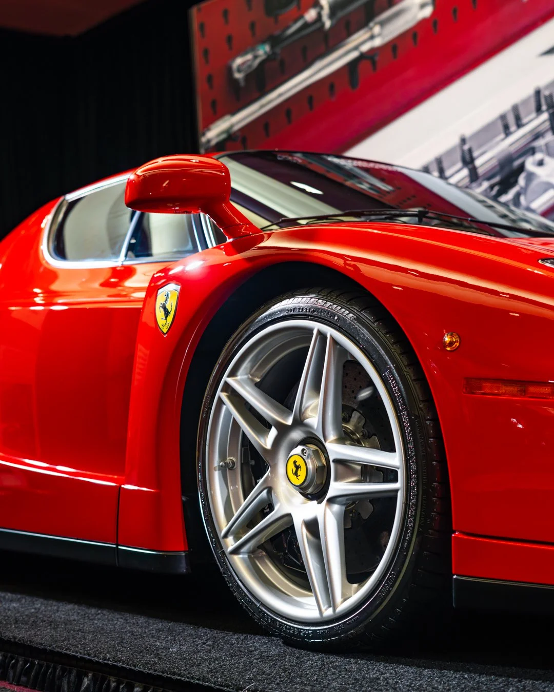 A close-up view of a red Ferrari sports car, showing the front left wheel and side mirror.