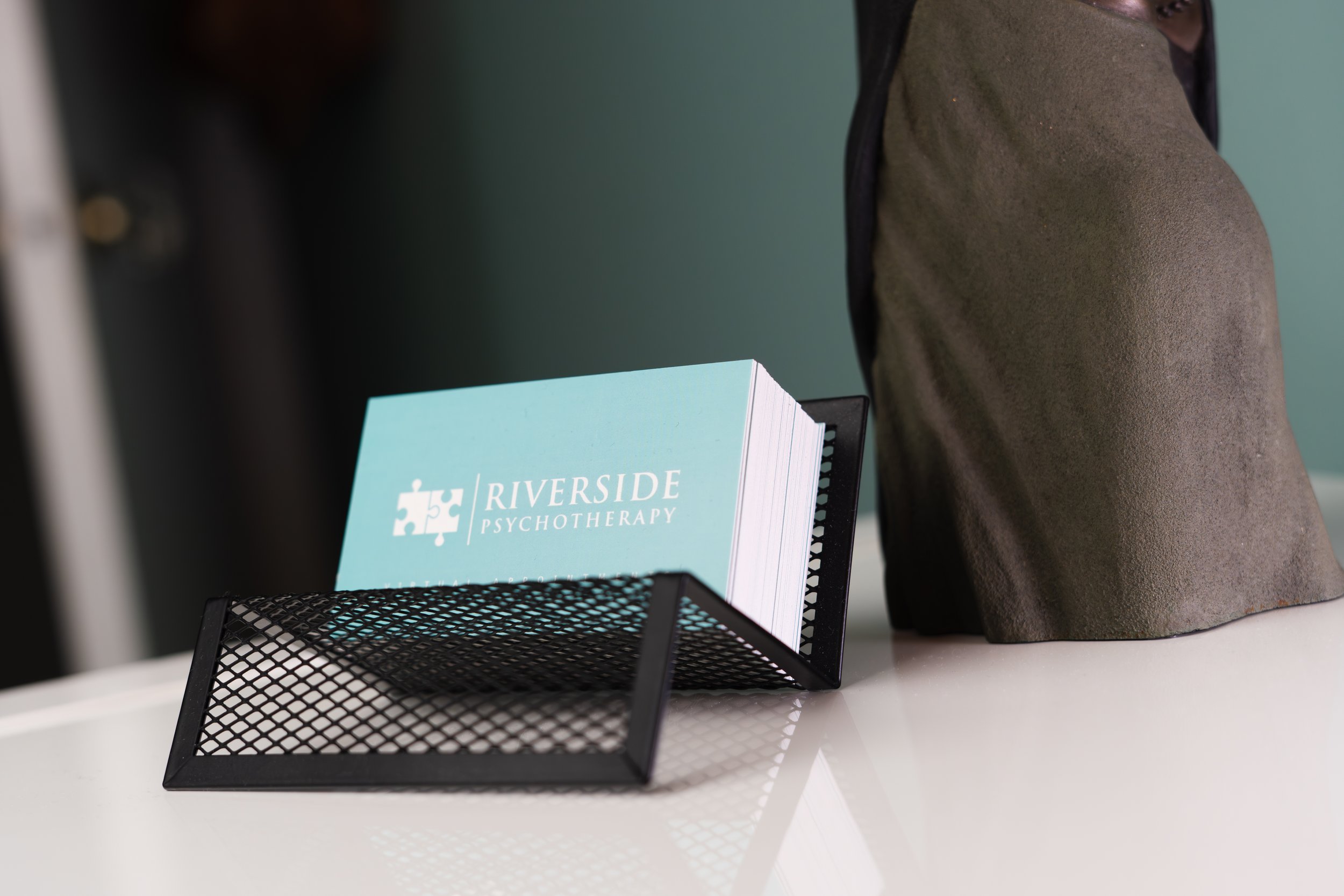 Business card holder with a card that reads 'Riverside Psychotherapy' and a bust sculpture on a white table.