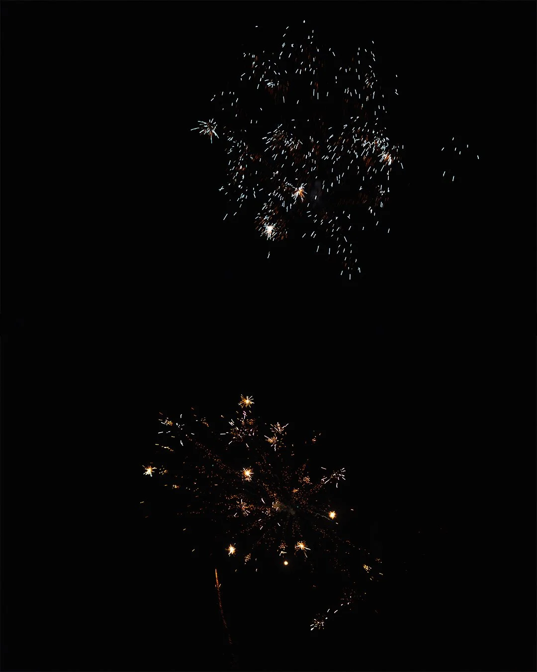 Two fireworks explosions lighting up the night sky with sparks and trails against a dark background.