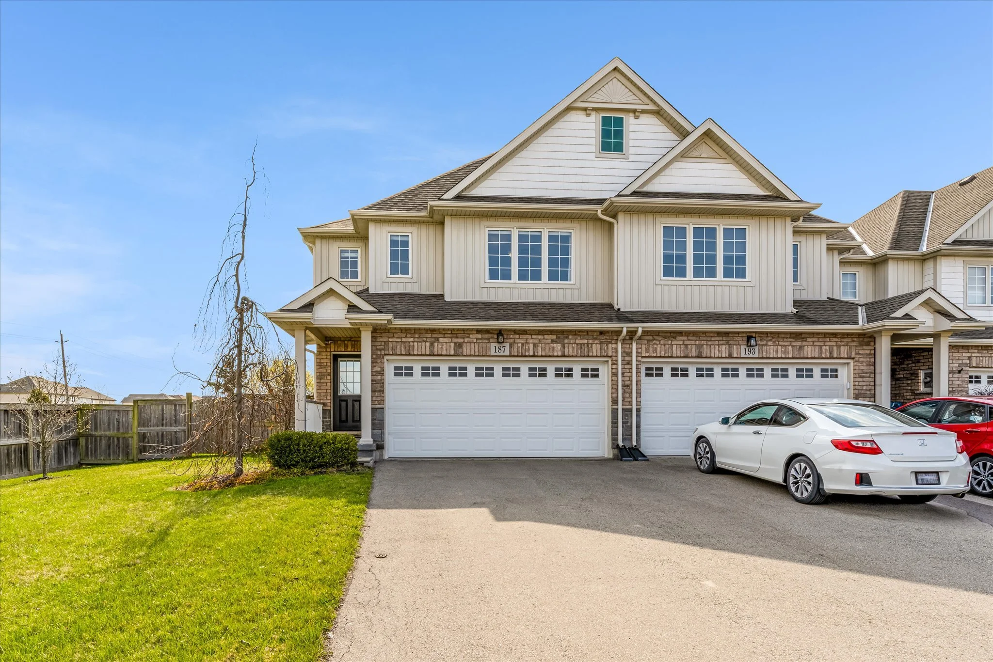 Front view of a two-story townhouse with a white garage door, brick and beige siding exterior, and a white car parked in the driveway.