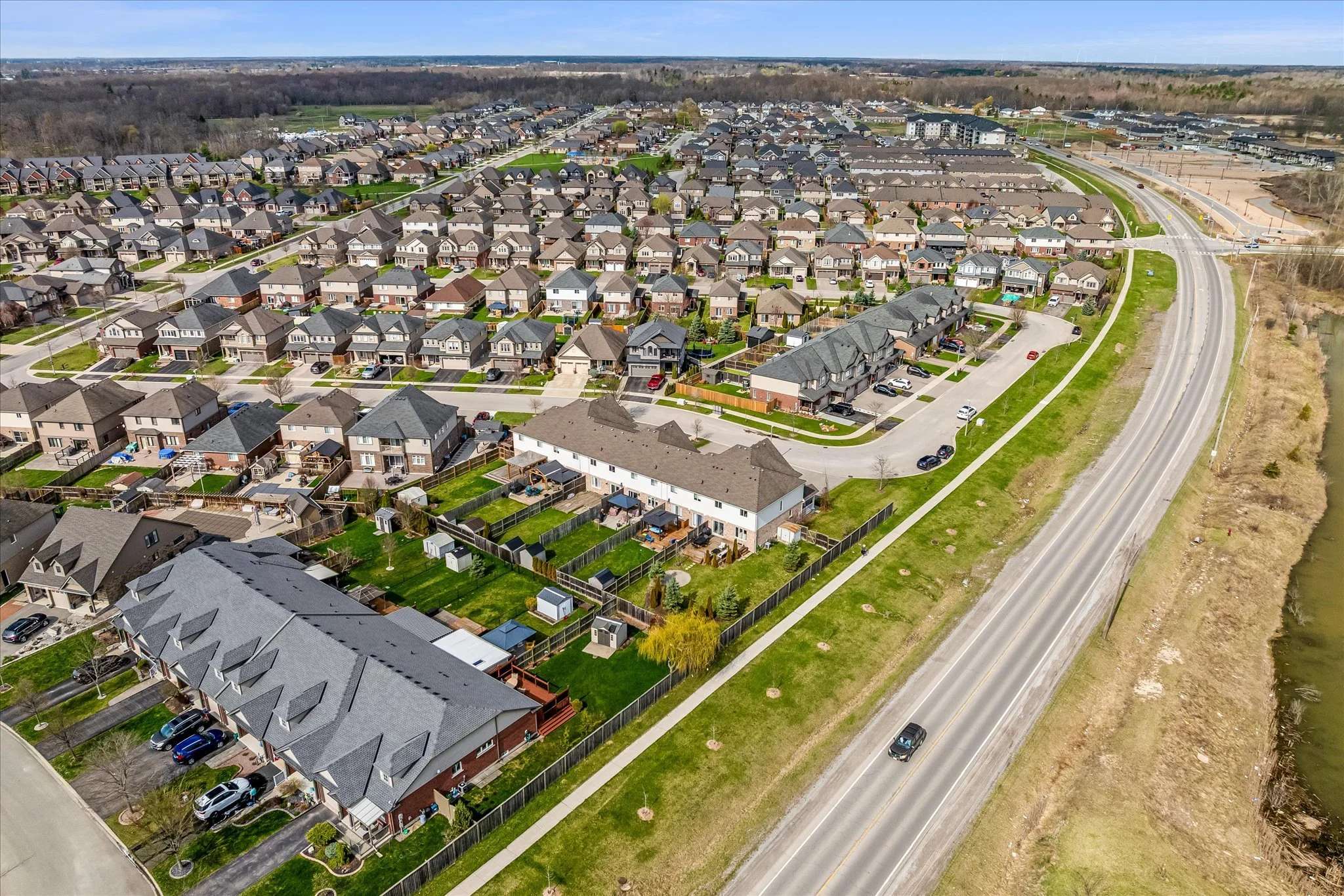 Aerial view of a suburban neighborhood with rows of houses, some with fenced yards, and a road running along the right side next to a waterway