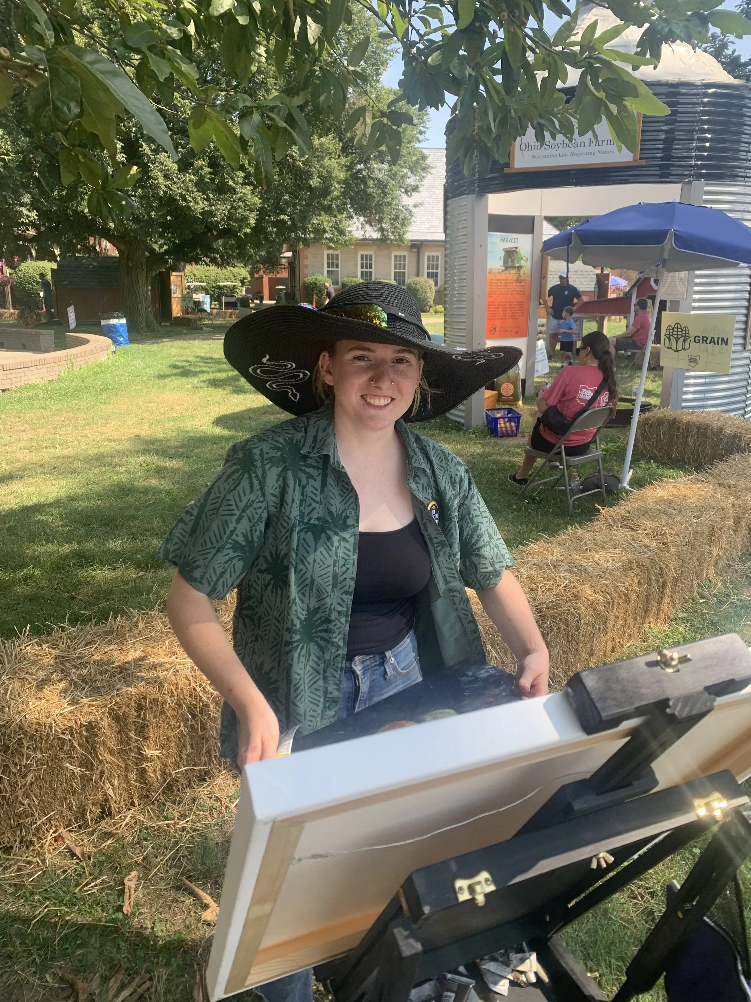 Makaila, the artist, painting outside with an easel in the foreground.