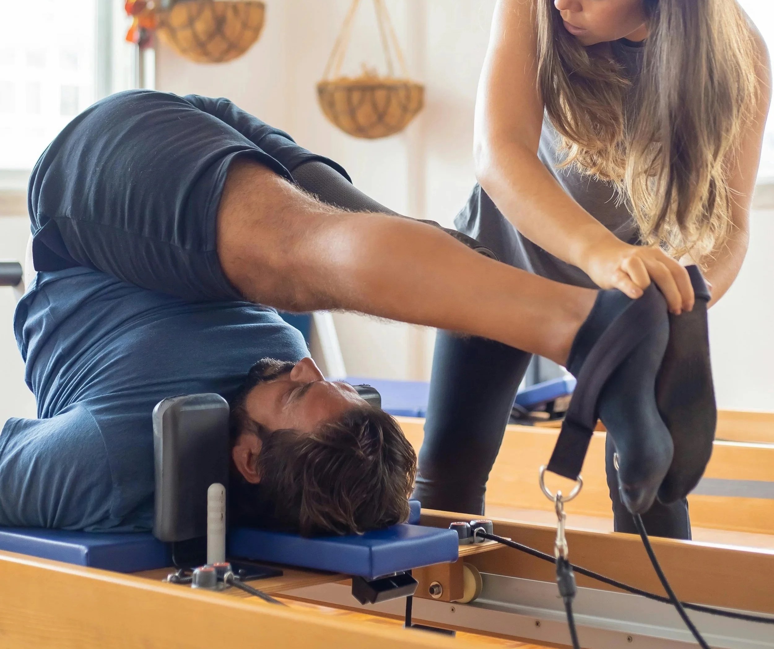 A man lying reformer/cadillac apparatus performing a pilates rollup exercise to strengthen the core area as part of a sports/athletic conditioning program.