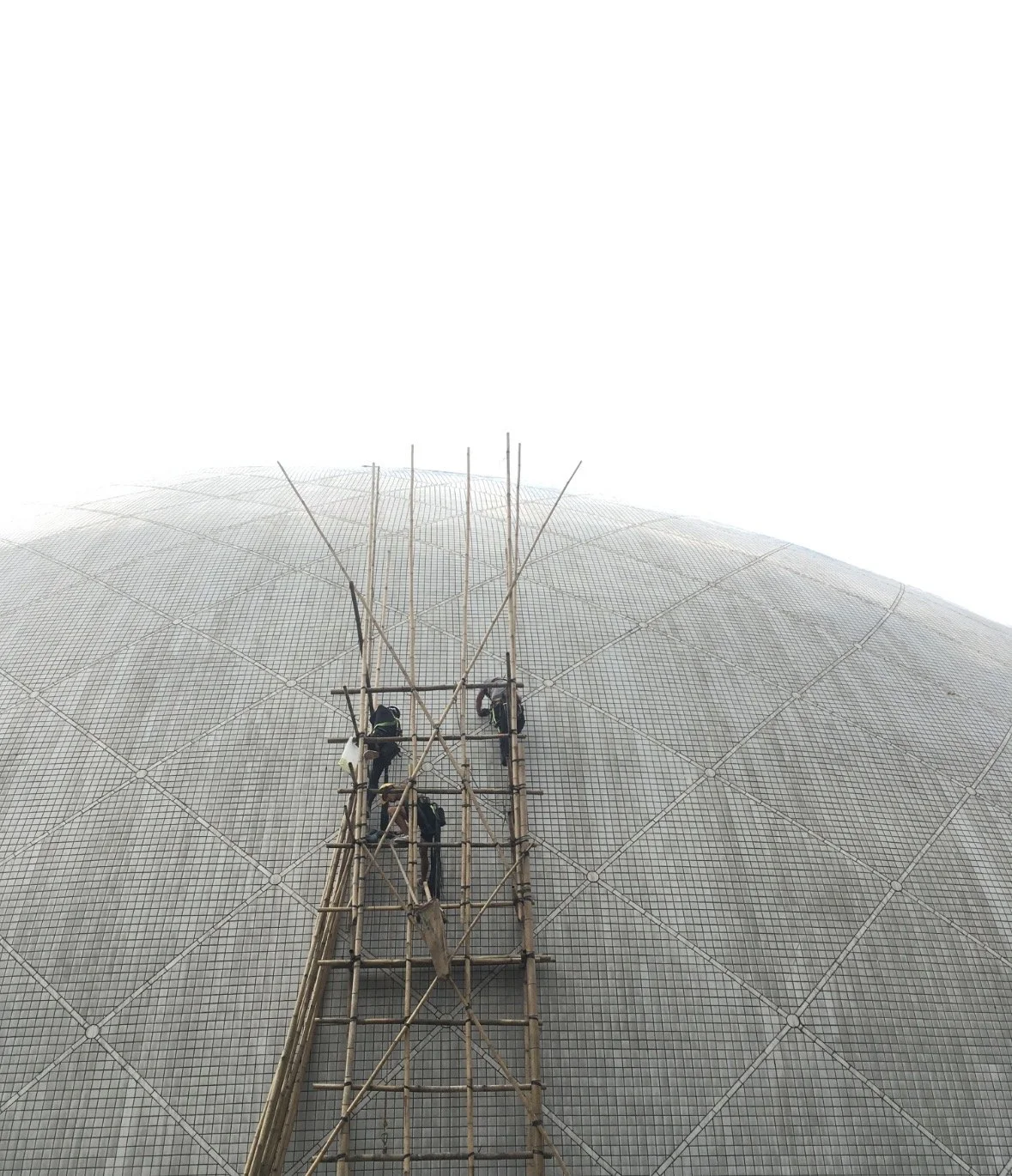 Workers on bamboo scaffolding inspecting or repairing a large domed structure with a tiled facade.