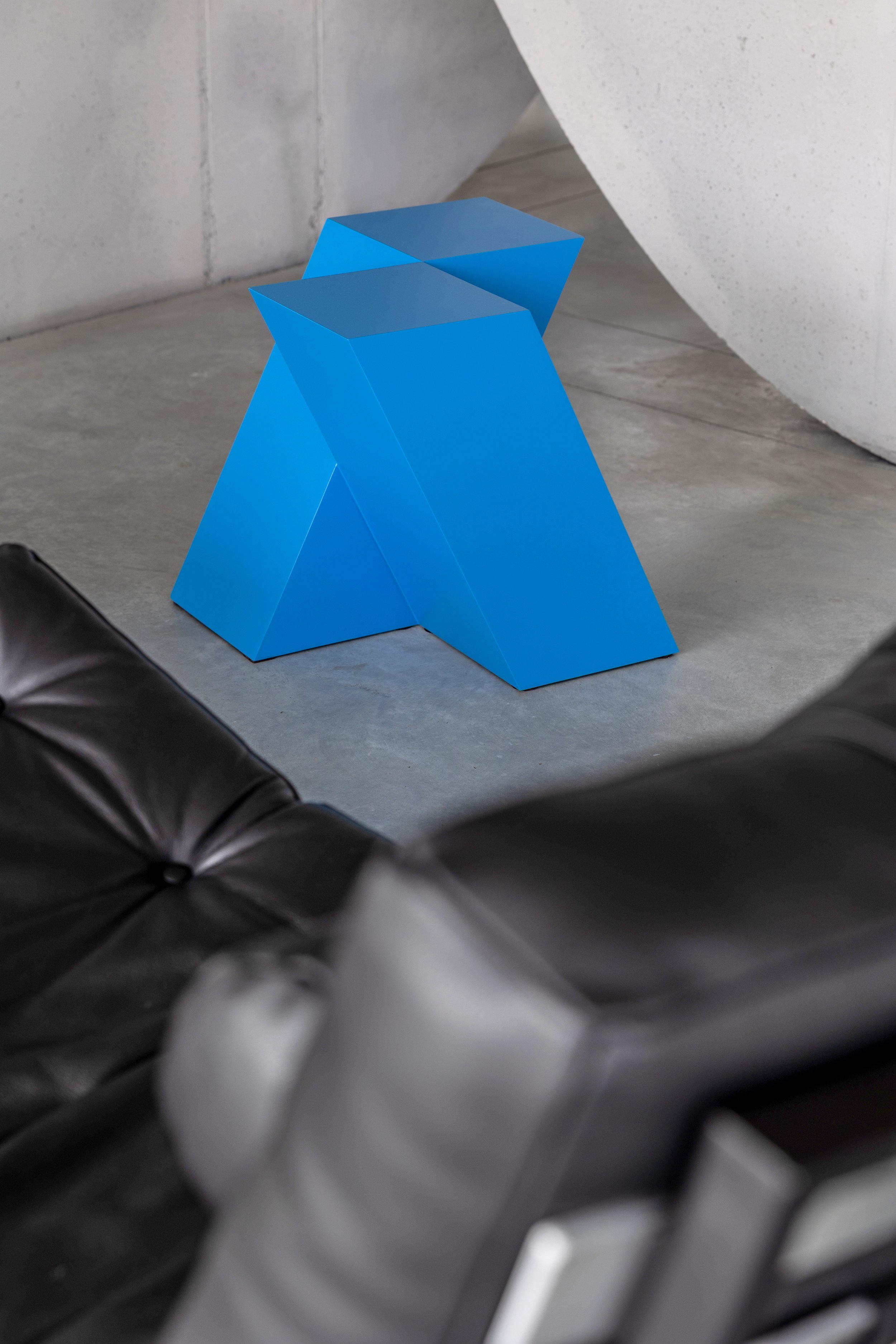 Blue geometric stool with angled sides in a modern interior space.