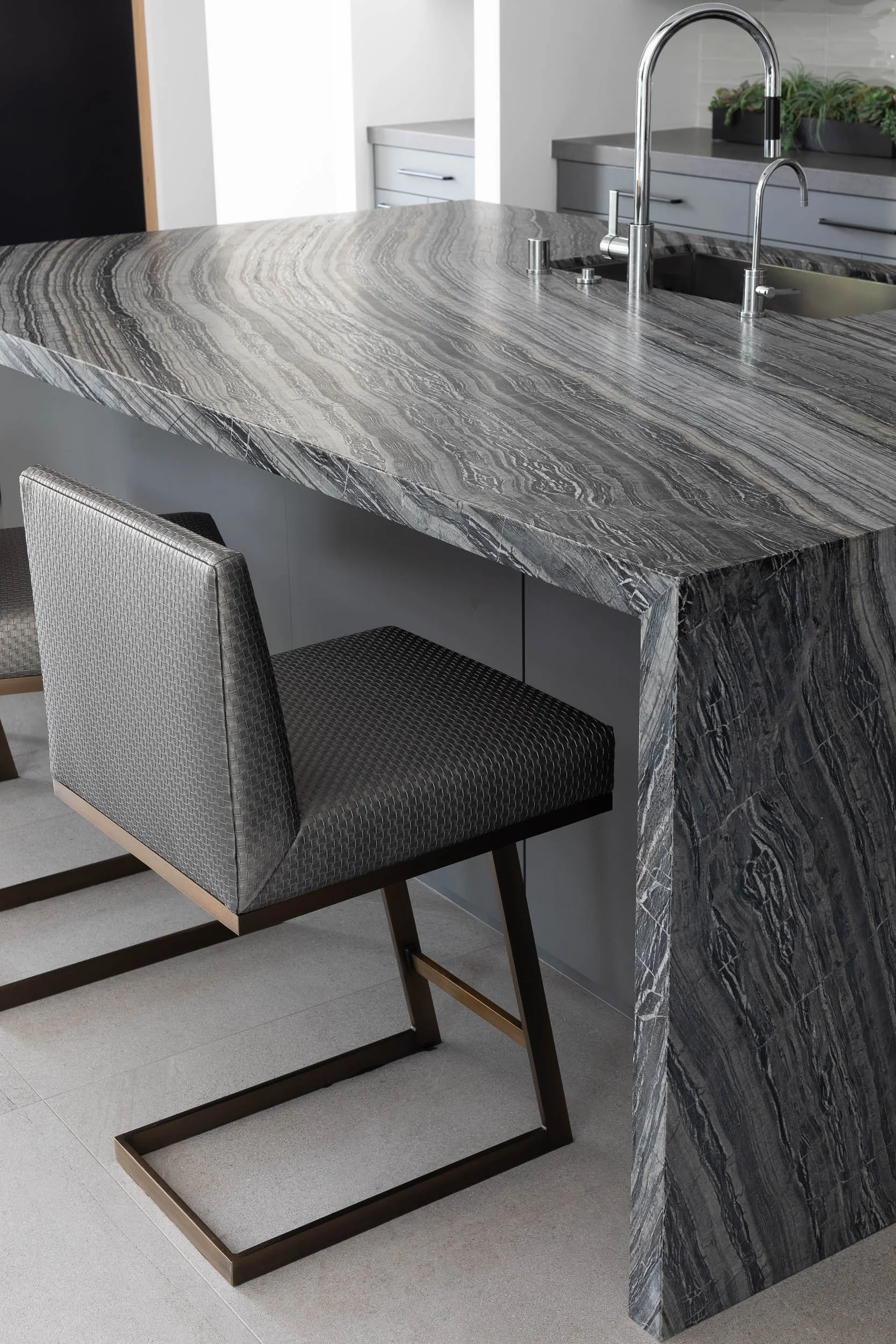 Modern kitchen island with a gray and white patterned marble countertop and matching side panel, with a gray upholstered chair with black metal legs positioned underneath.