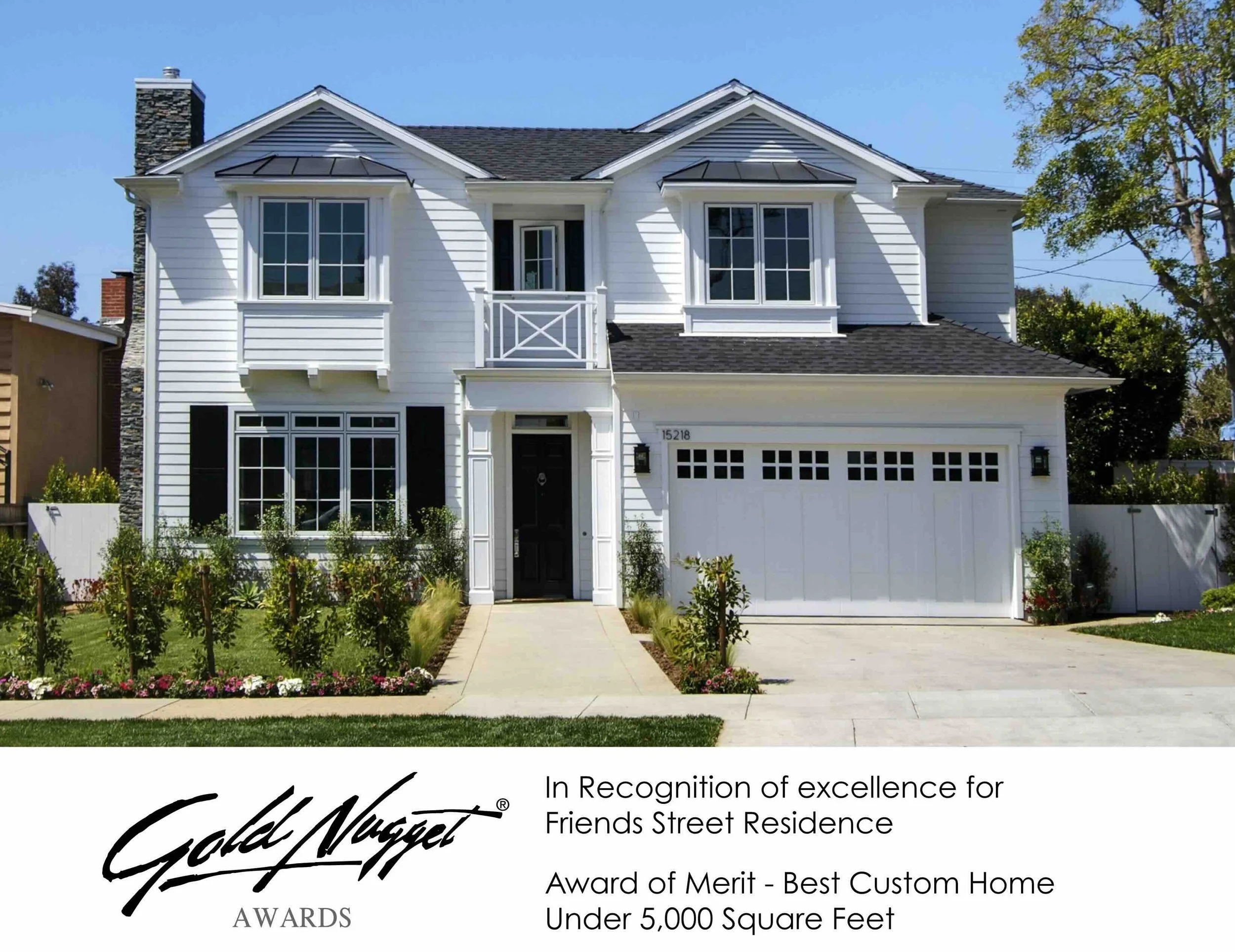 White two-story house with black shutters, a balcony, and a two-car garage, surrounded by a landscaped yard with flowers and bushes in front.