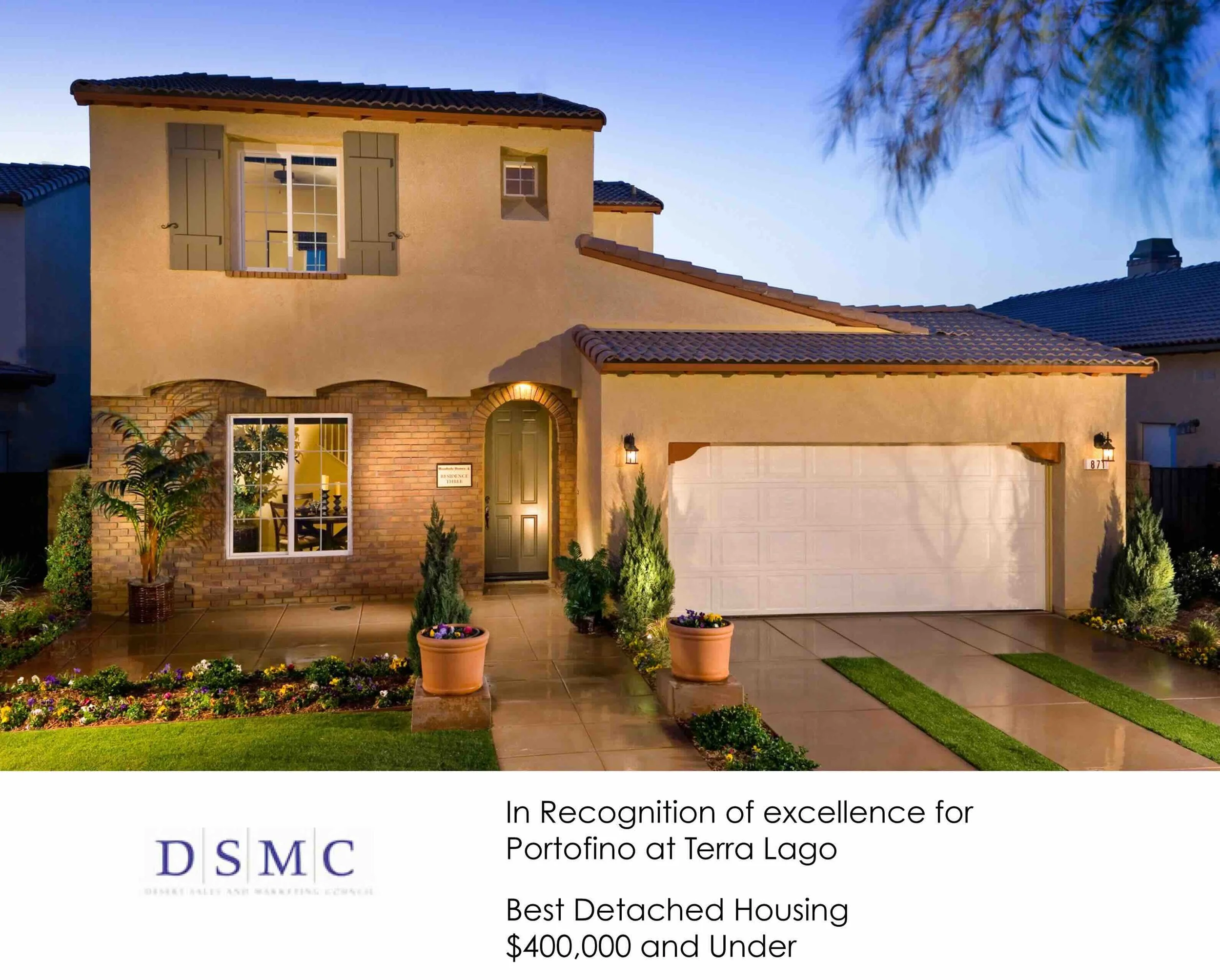 A two-story house with a beige exterior, brick accents, and a tiled roof, featuring a garage, front door, and well-maintained garden, under evening sky.